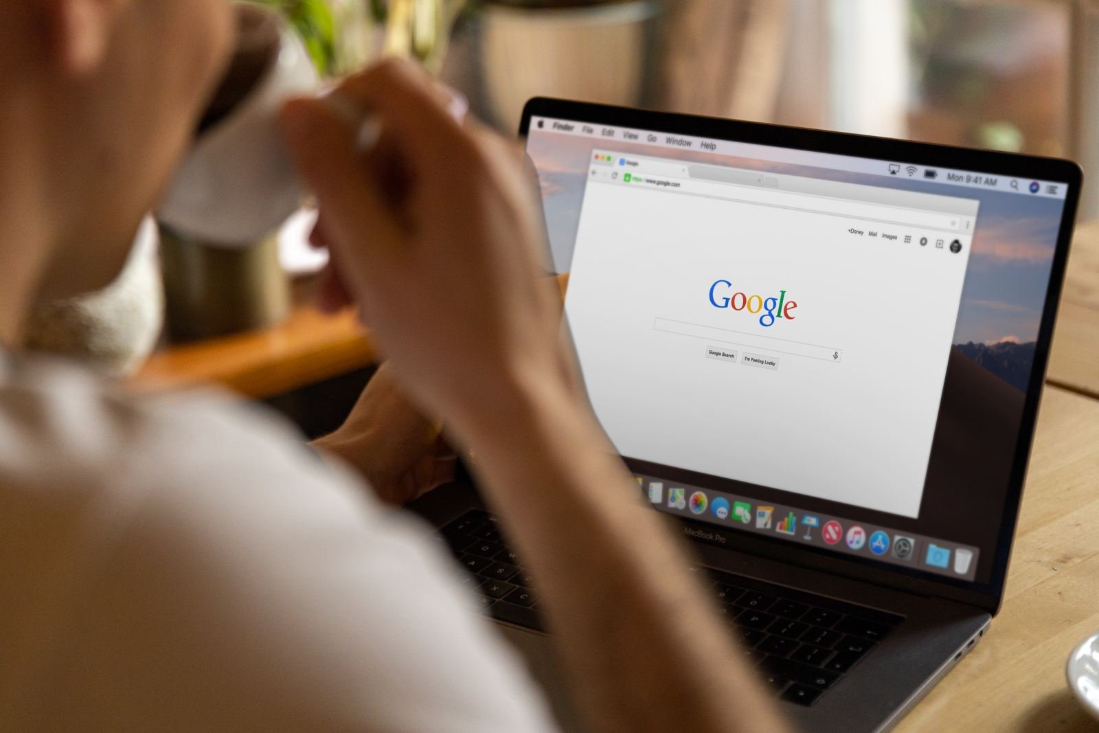 A person holds a mug while looking at a Google search page on a laptop