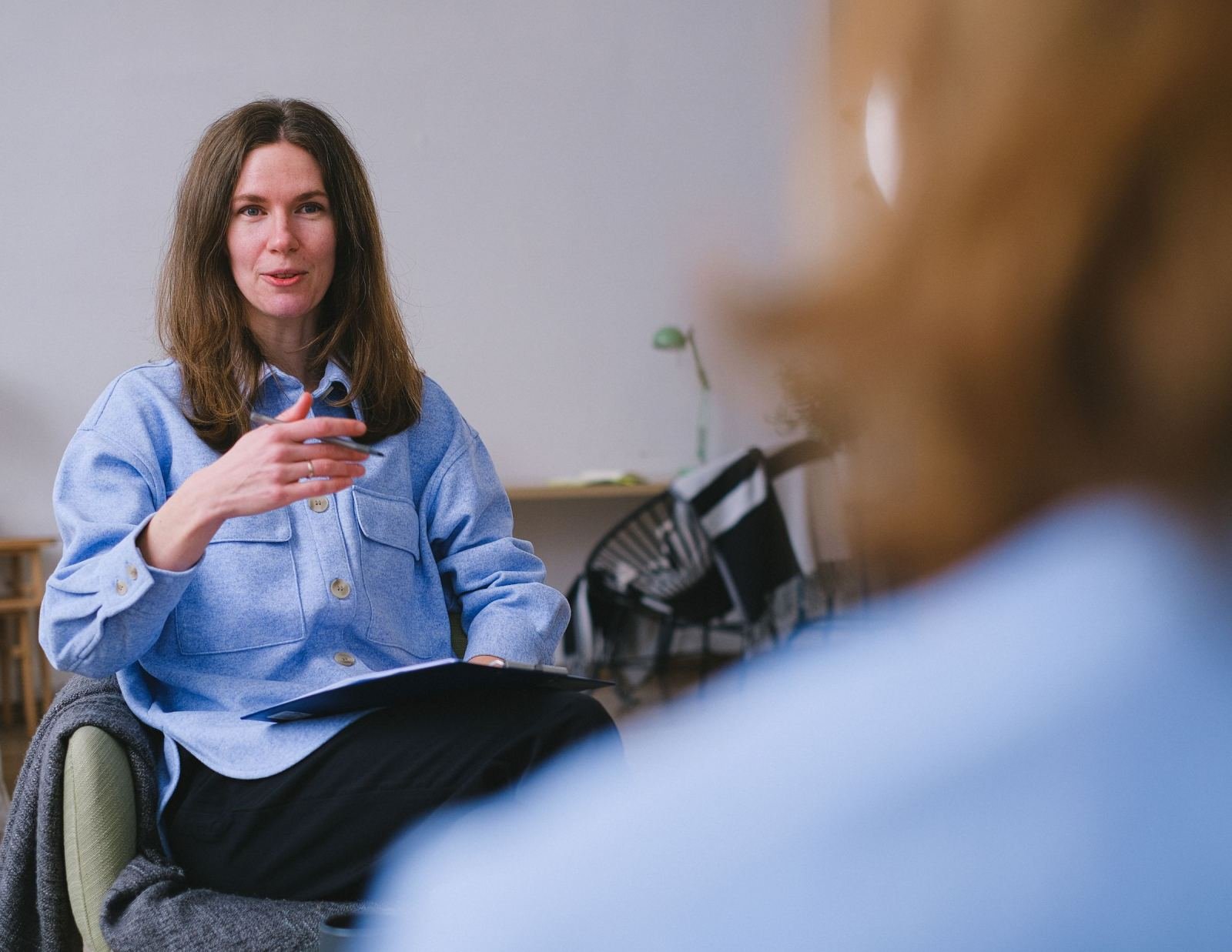 A woman wearing a blue shirt talks and uses her hands to speak with someone in a well-lit room