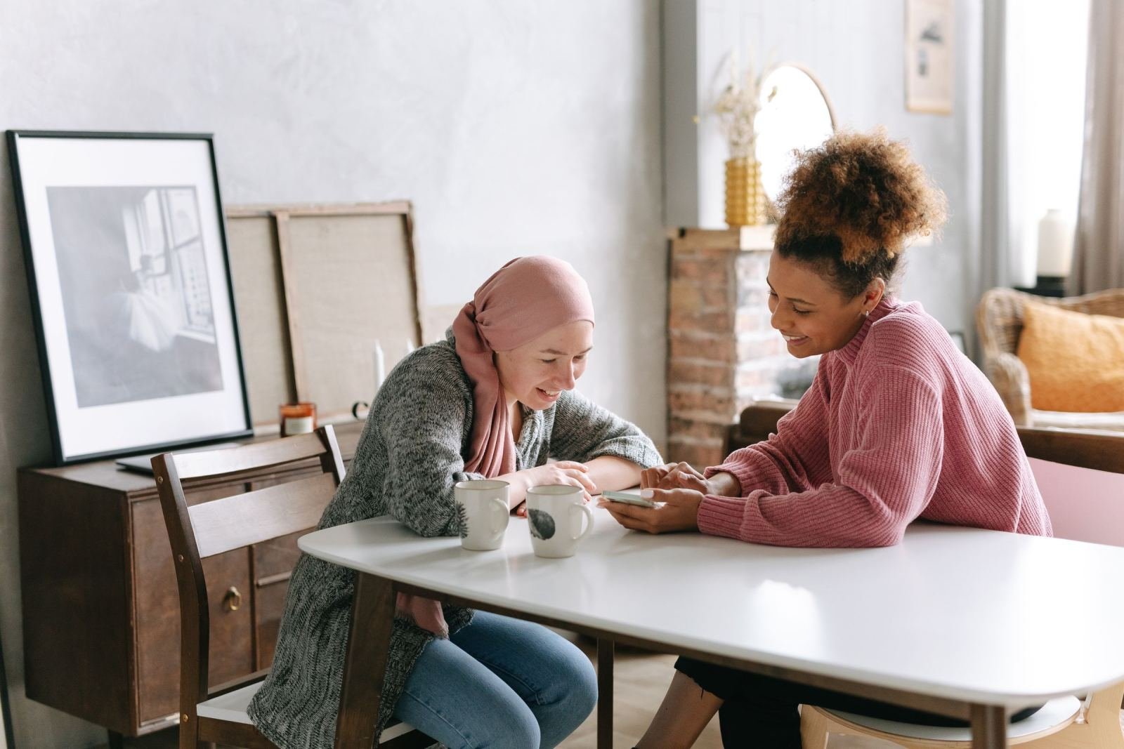 Two women sit at a table together looking at a smartphone