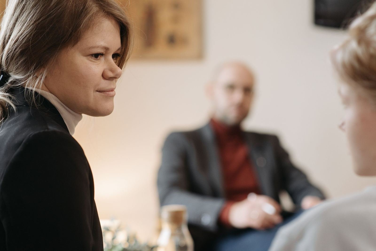 A woman in a black blazer speaks with others in a professional setting