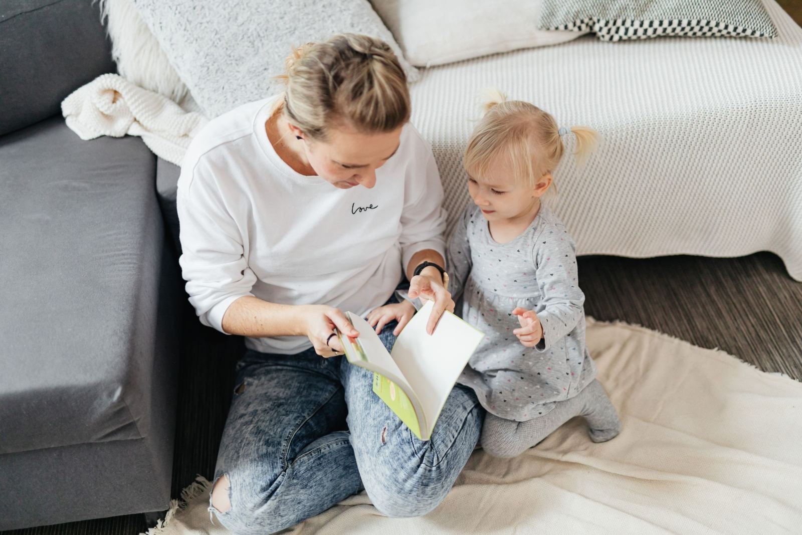 A mother and her small child sit on a floor mat, sharing a storybook.