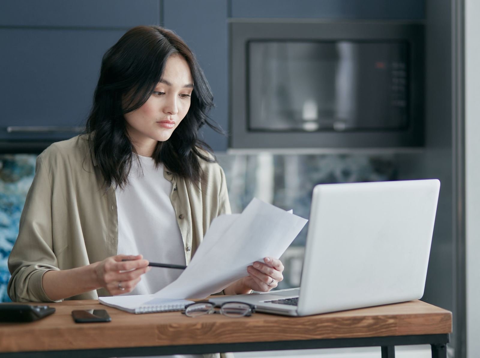 A woman reviews documents while sitting at a table with a laptop