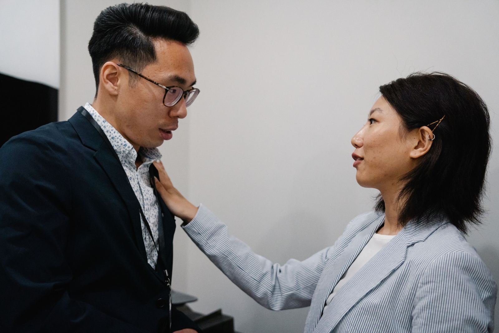 A woman in a striped blazer talks with a man in a dark blazer in a bright office