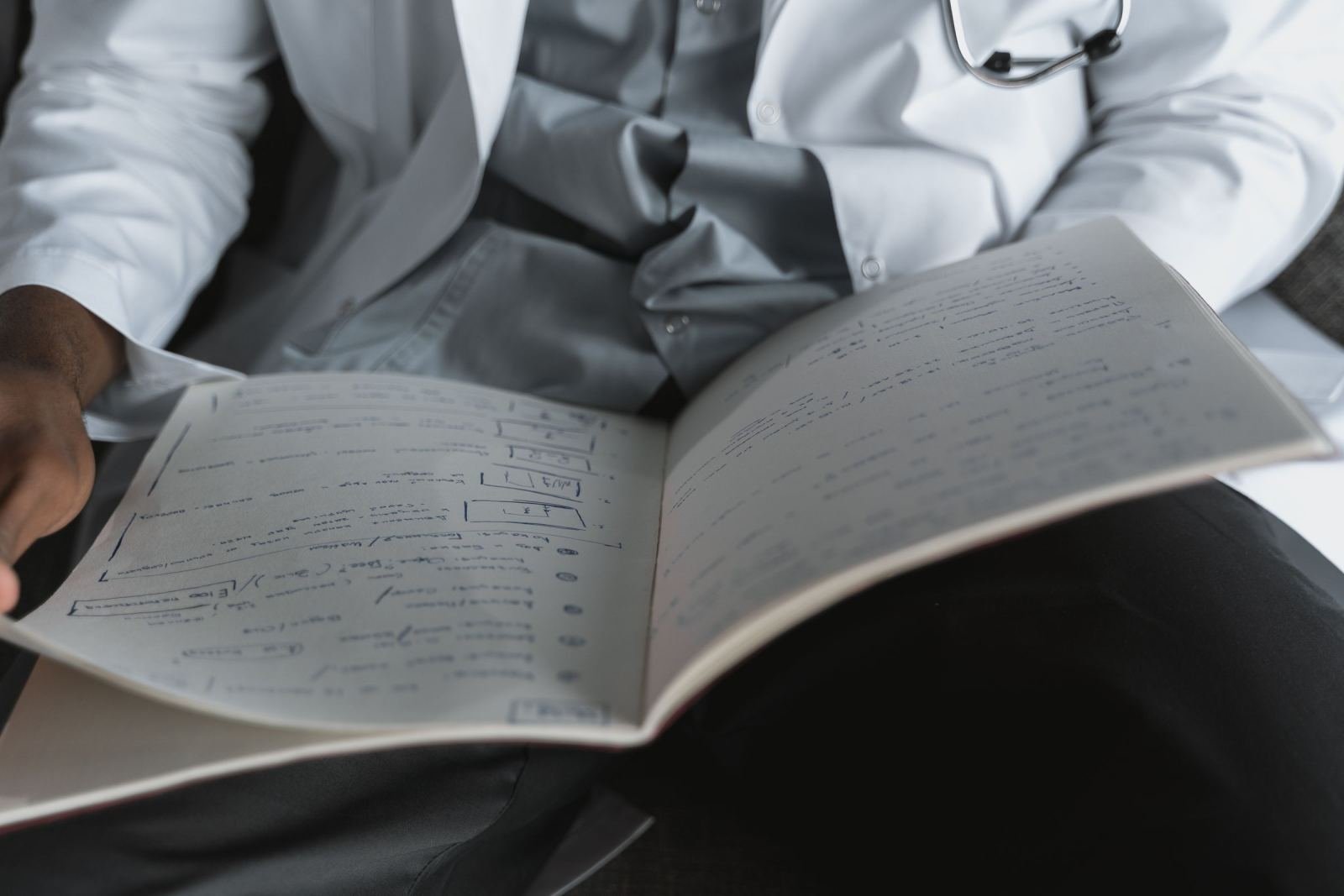 A clinician in a white coat holds an open notebook with handwritten notes