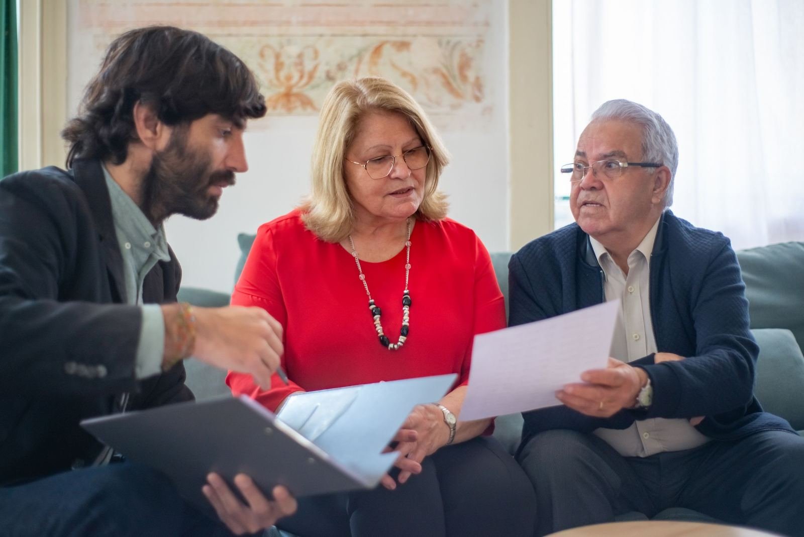 A man holding a folder talks to a woman and an older man. They are looking at a paper.
