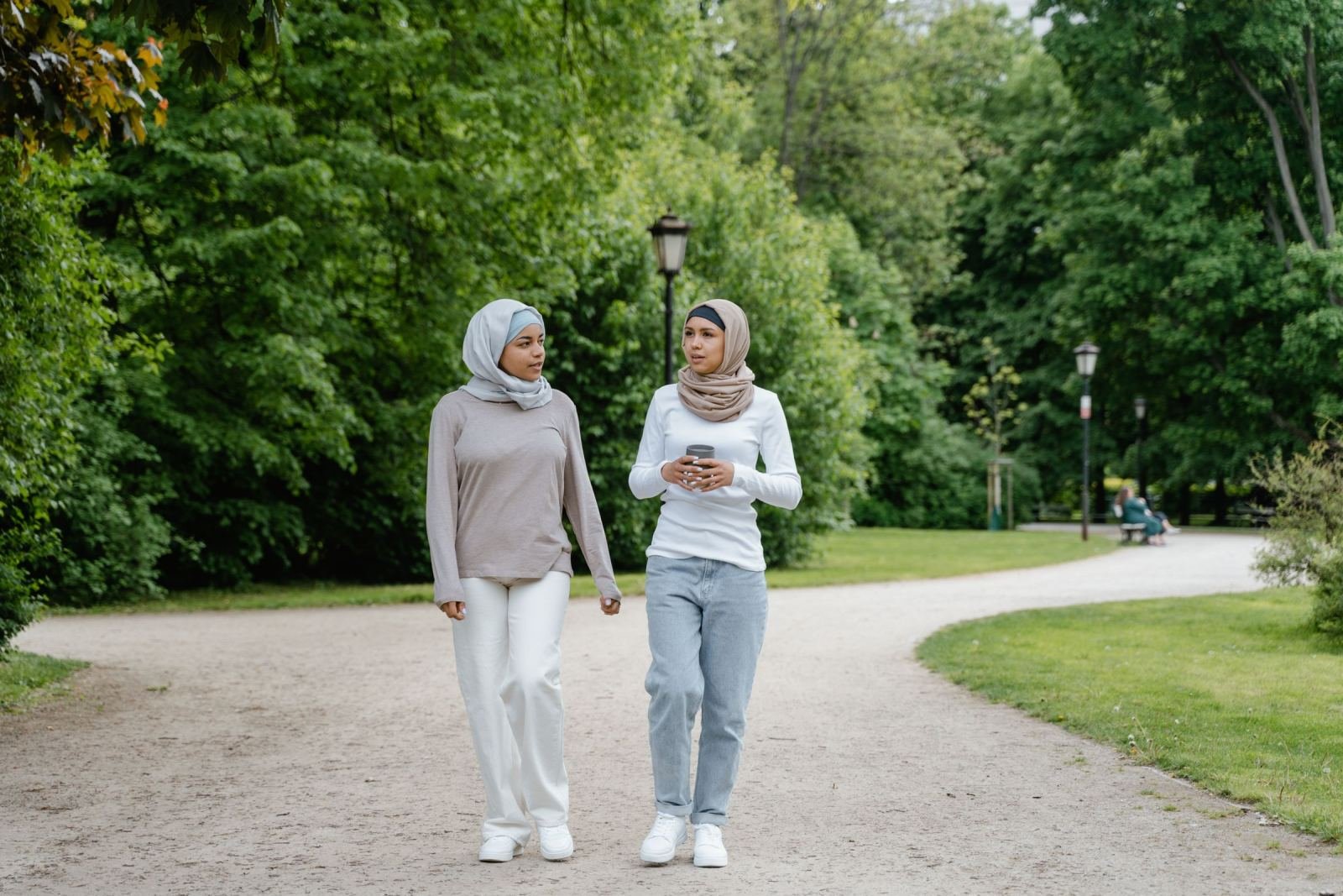 Two women in hijabs walk and speak on a trail in the park.