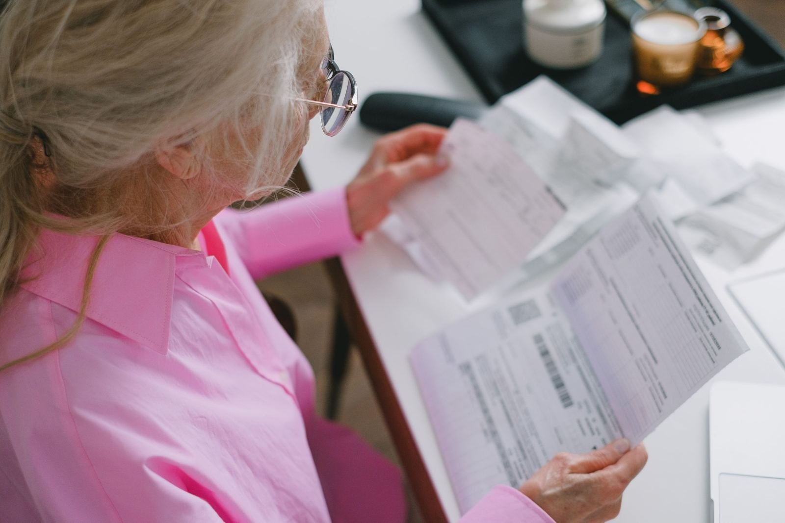 A senior lady in a pink top looks over papers on a white table