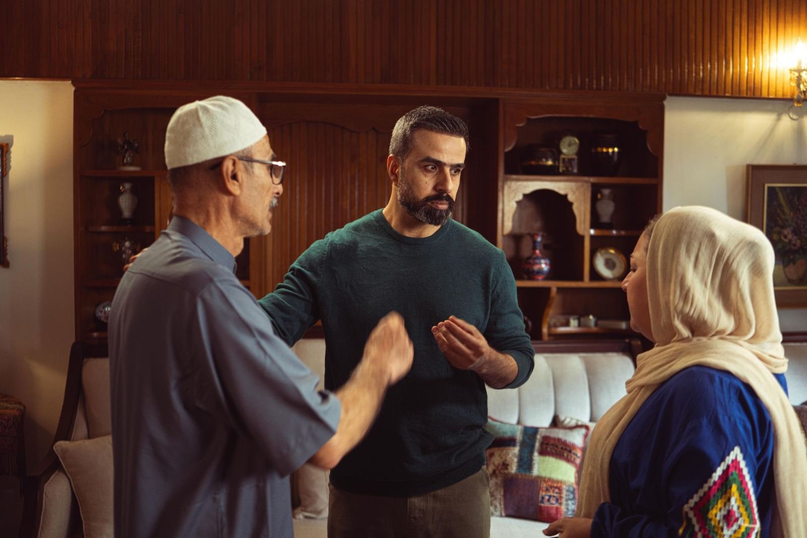 Three people talking together in a room with wood paneling and a white sofa