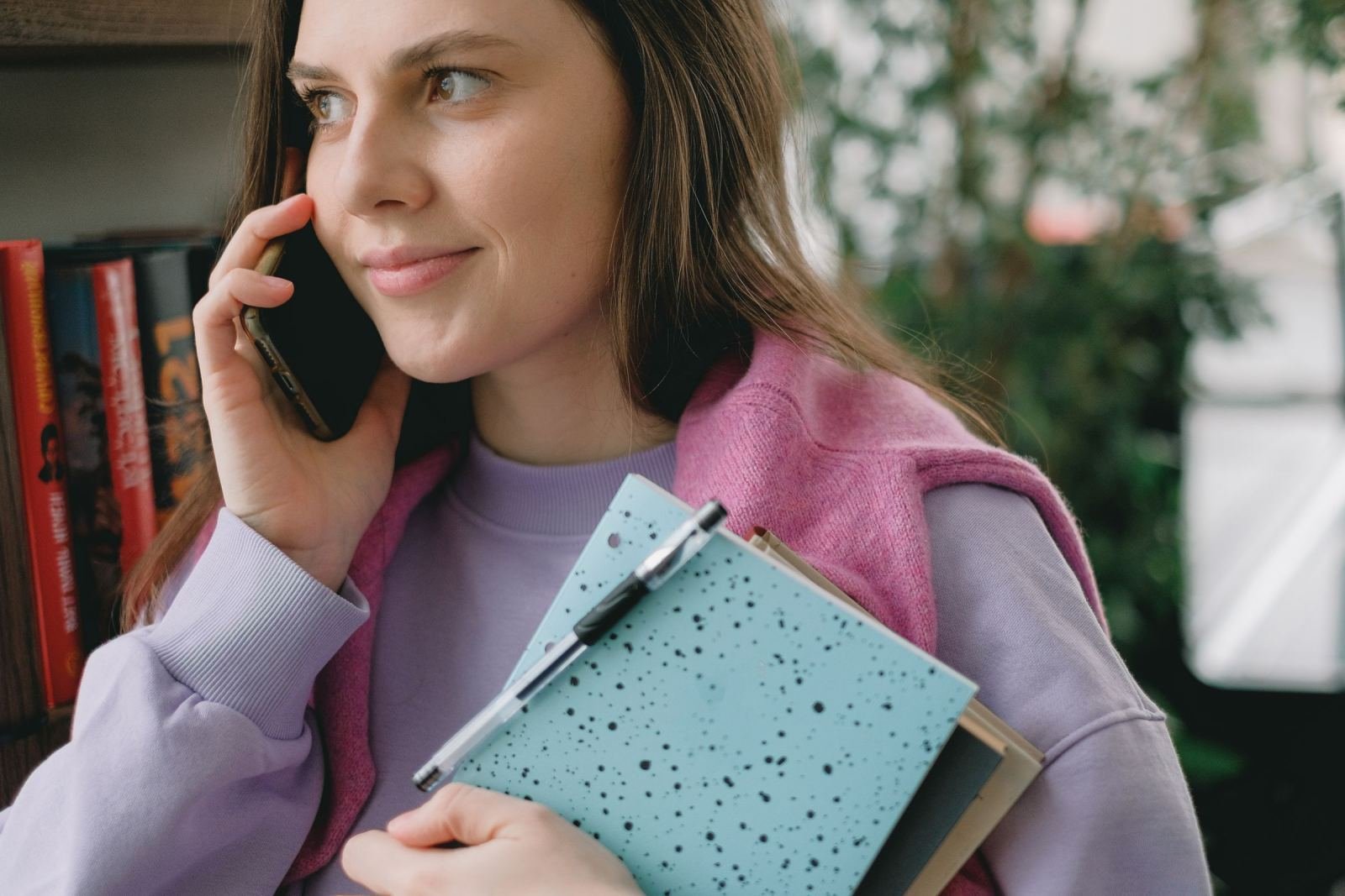 A woman on a phone call holding a blue notebook and a pen