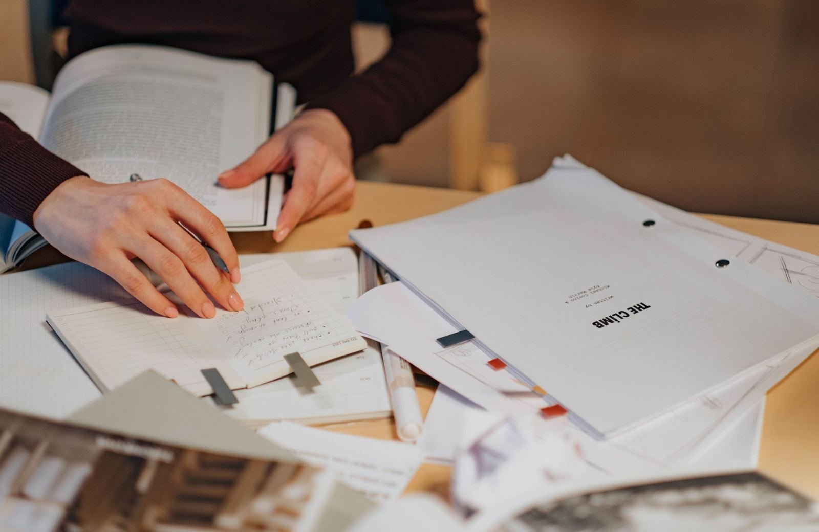 Hands of a person reviewing notes and books at a desk