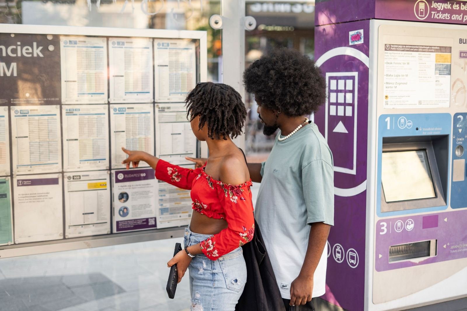 A woman points to a transit schedule while standing with a man at a bus stop