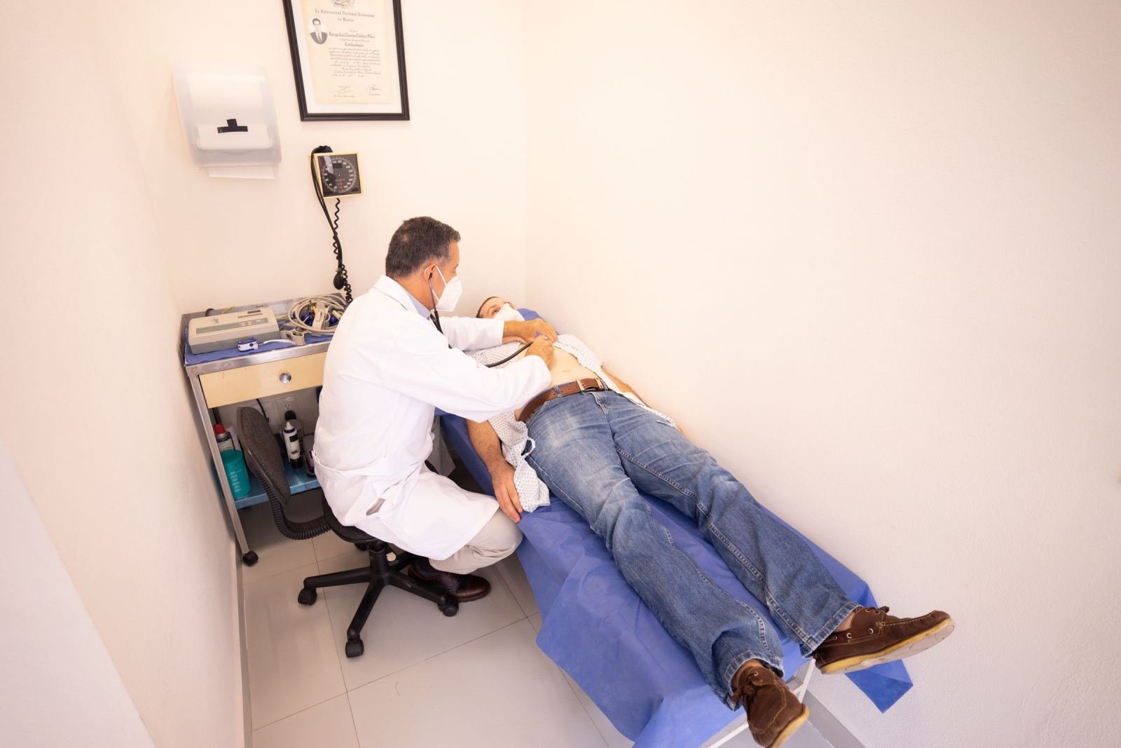A doctor in a white coat examines a patient lying on a medical table with a stethoscope