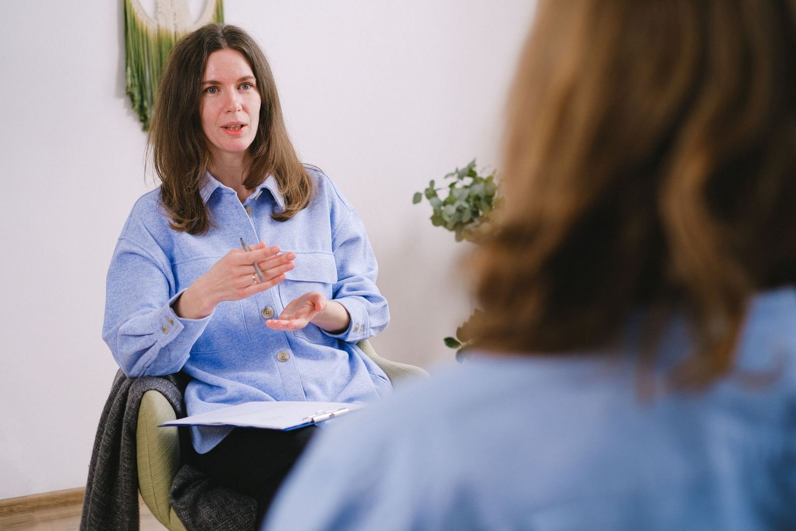 A woman wearing a blue shirt uses her hands to talk to someone else in a bright room