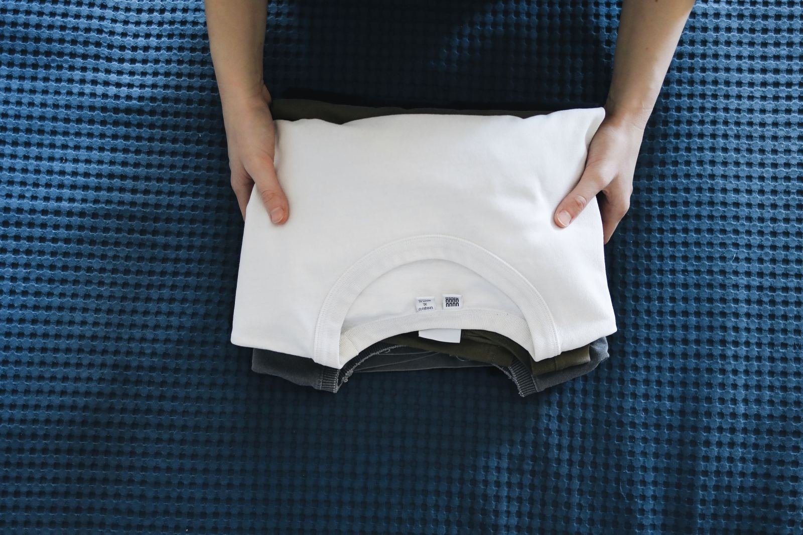 Hands holding a stack of folded clothes on a blue textured surface