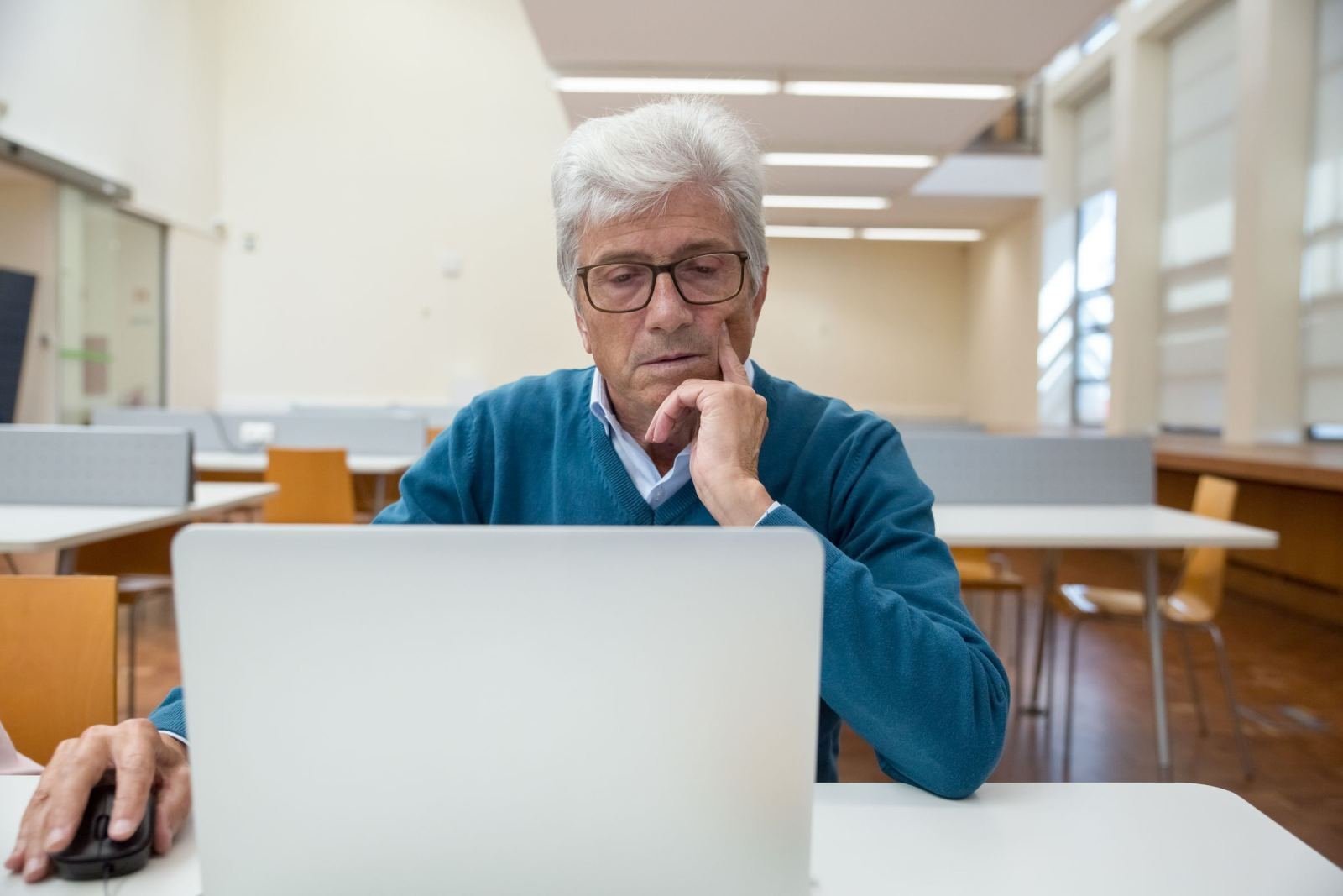 A man with glasses looks thoughtfully at a laptop screen