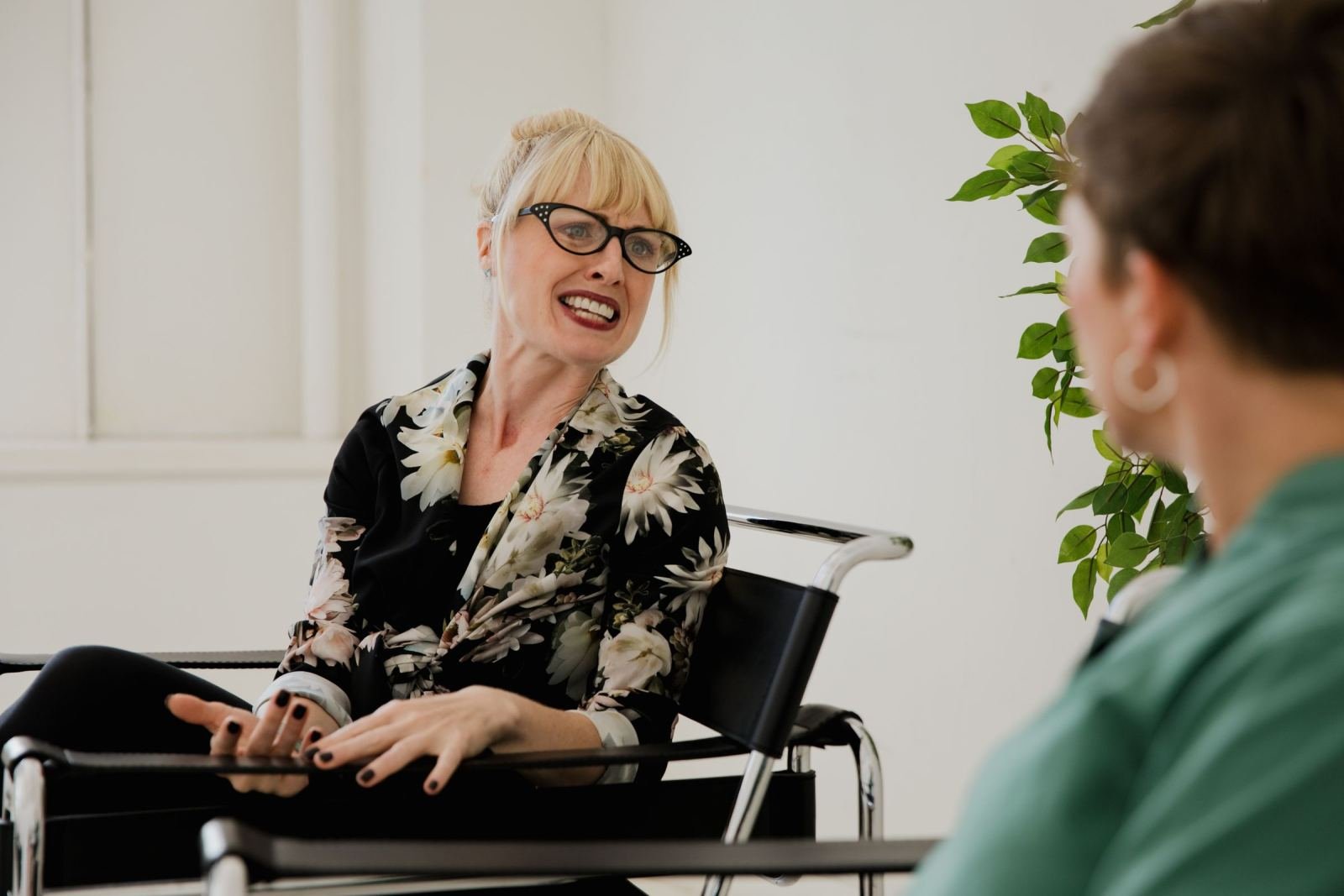 A woman wearing a floral blouse talks and uses hand gestures while in an office meeting.