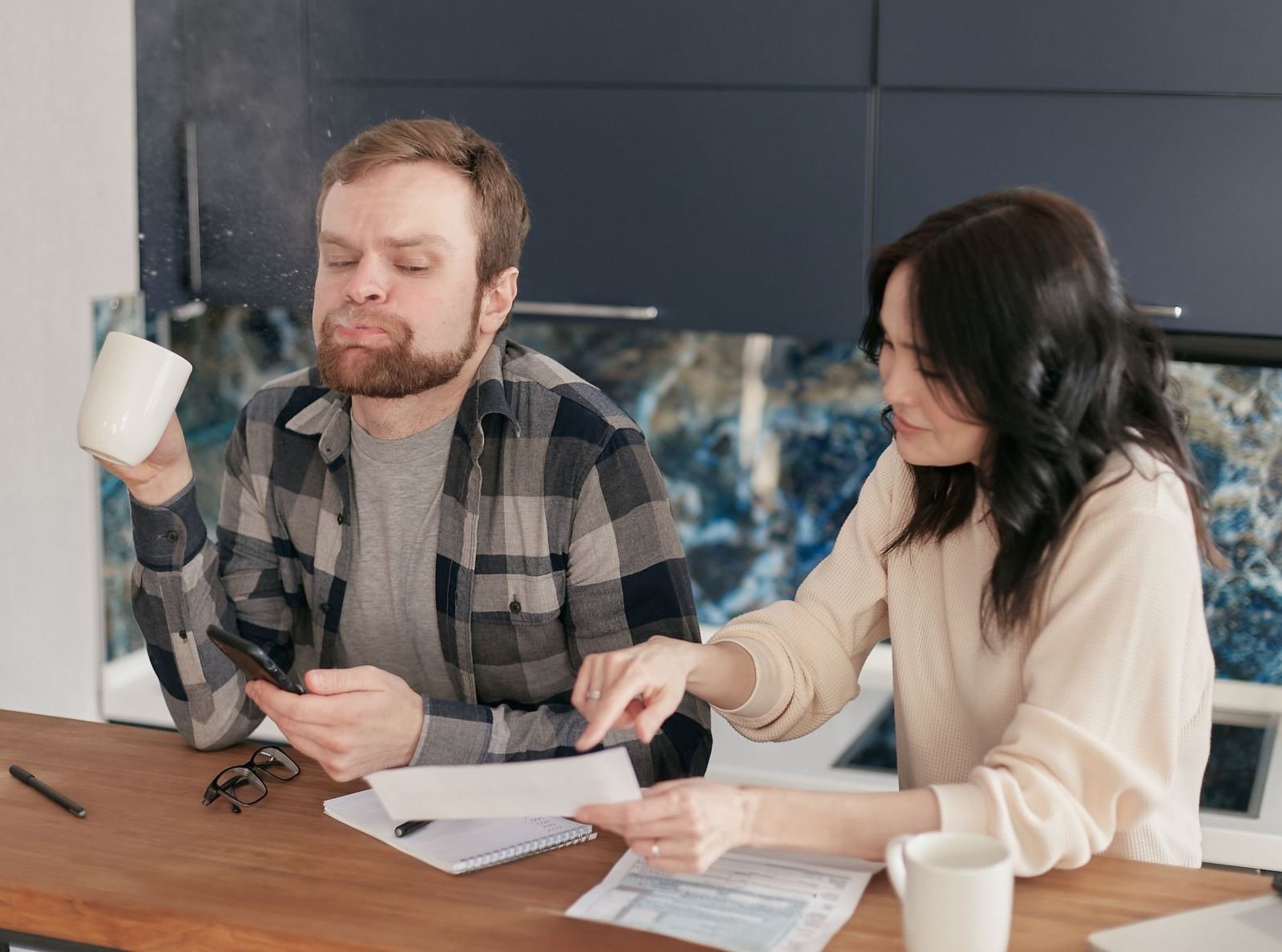 A man and woman review paperwork and a smartphone at a wooden table