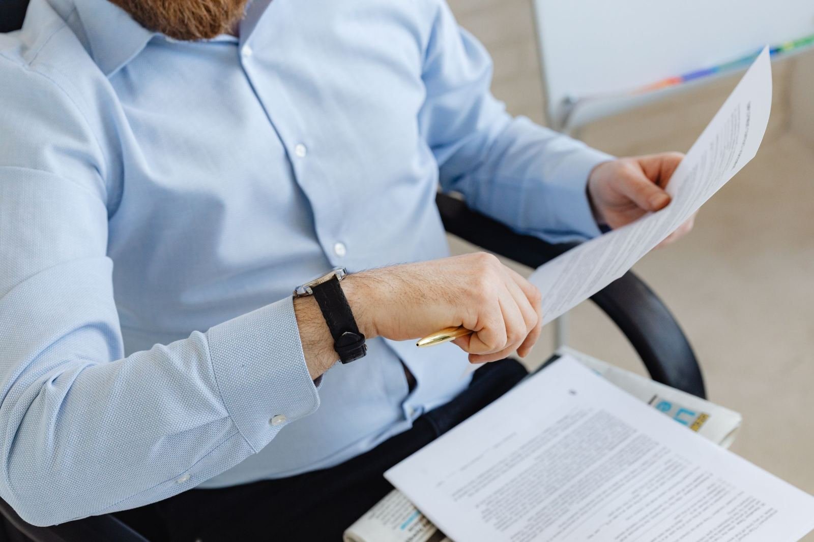 A person in a blue shirt holds a document and a pen in an office