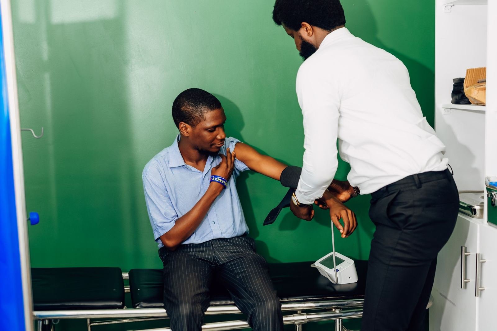 A doctor checks the blood pressure of a man sitting on an exam table