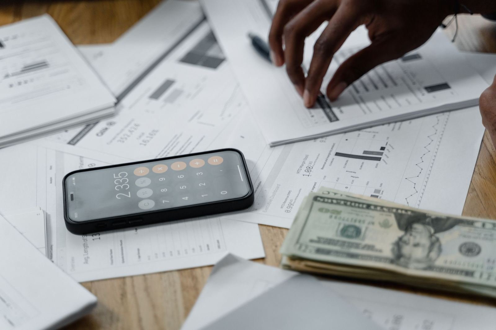 A person reviews financial documents with a calculator and cash on a table