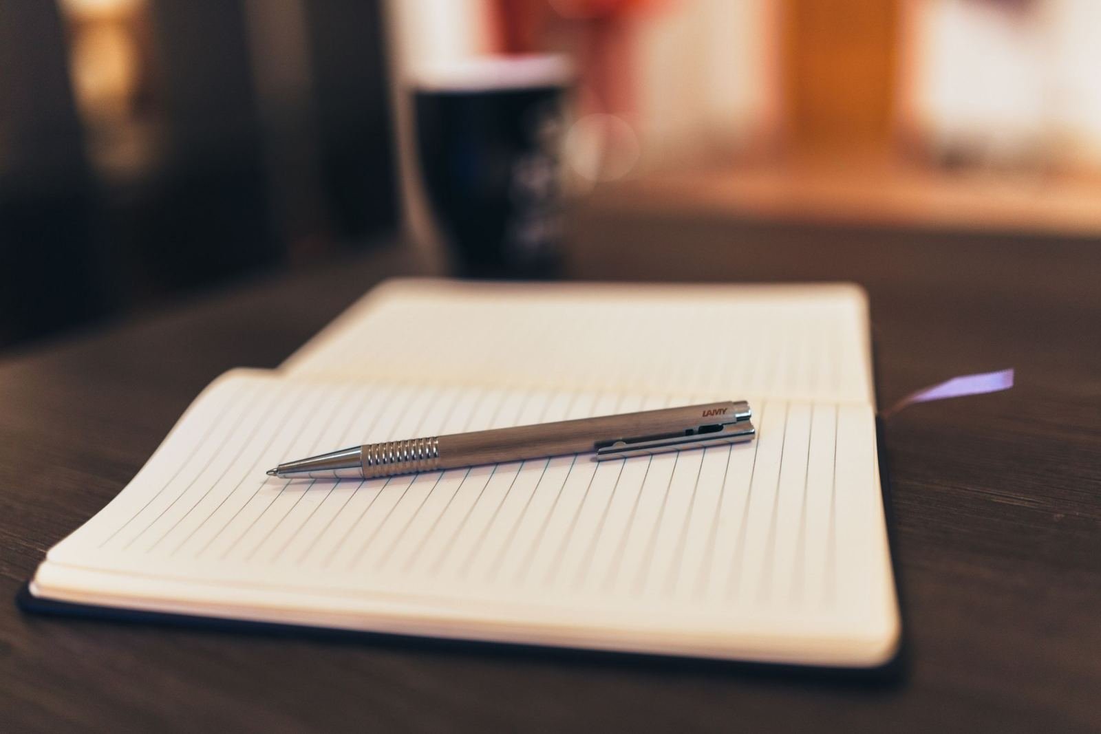 A silver pen resting on an open lined notebook on a dark table