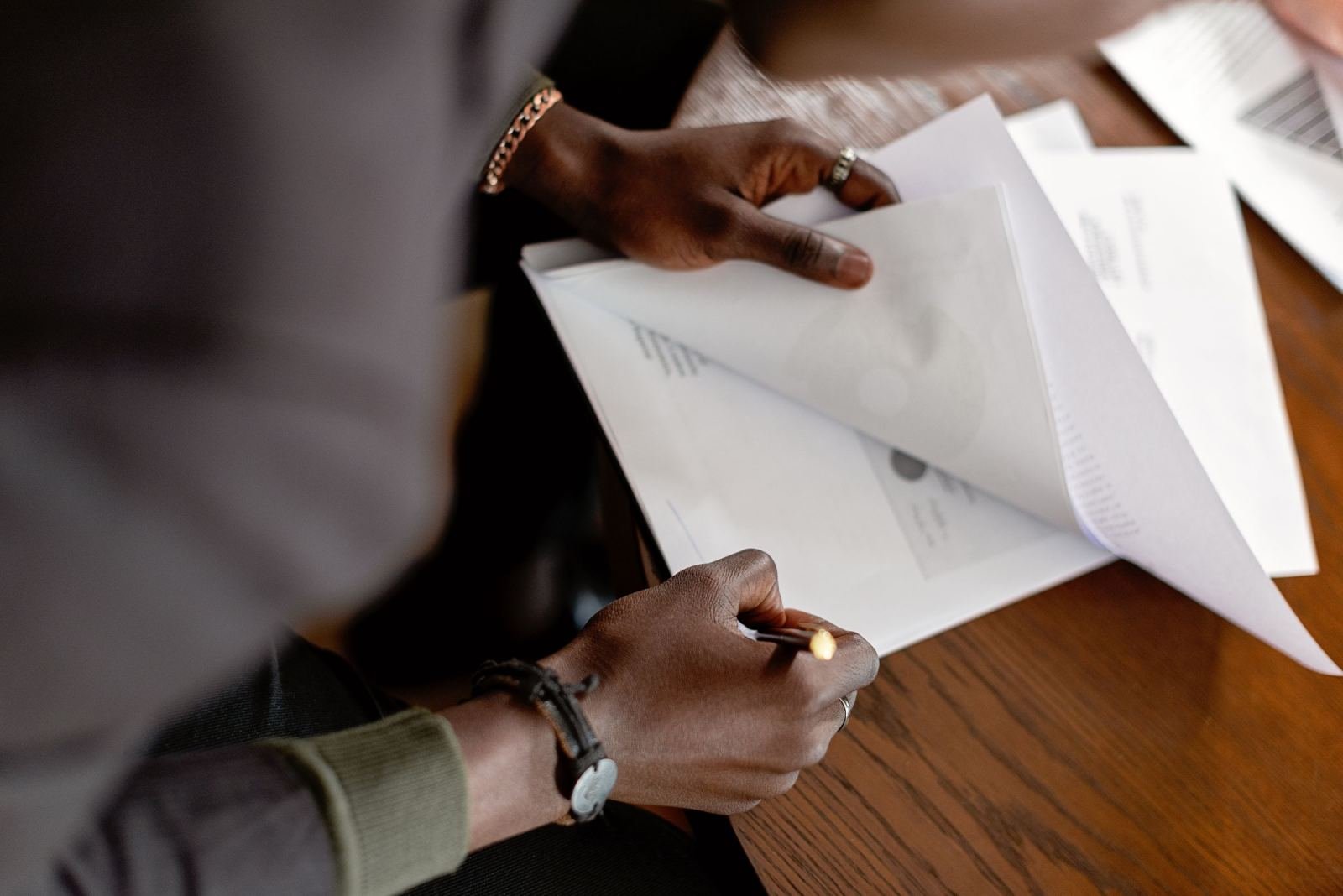 Two people review and sign paperwork at a wooden desk