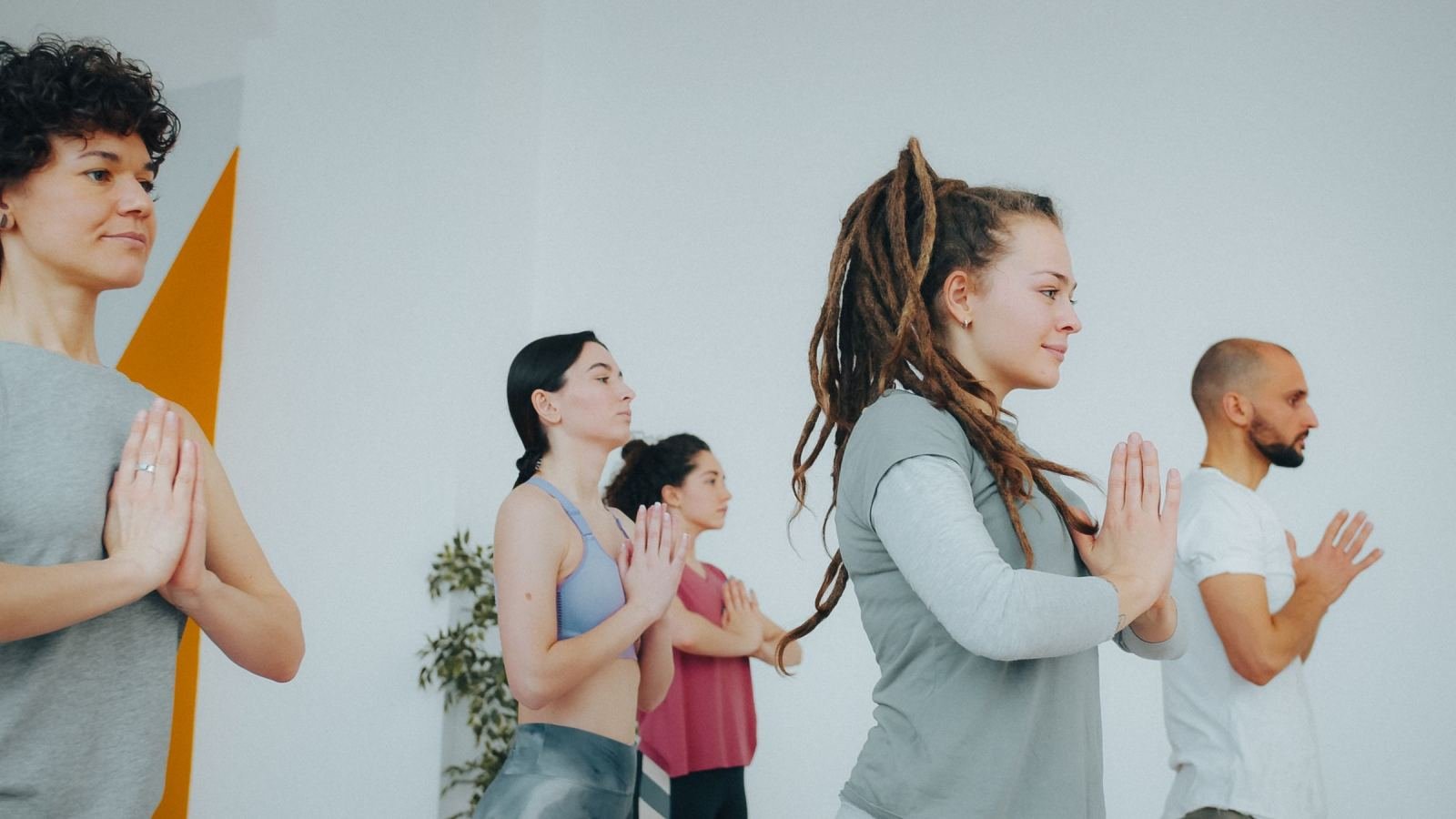 Four adults in athletic wear stand with their hands in a prayer position in a bright studio
