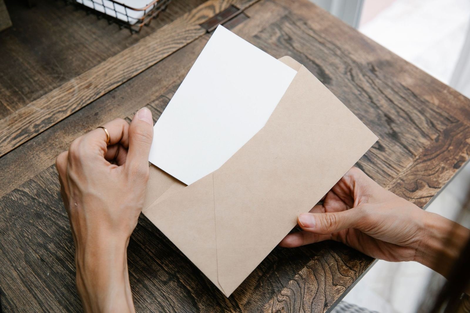 Hands holding a blank white card and a brown envelope on a wooden table