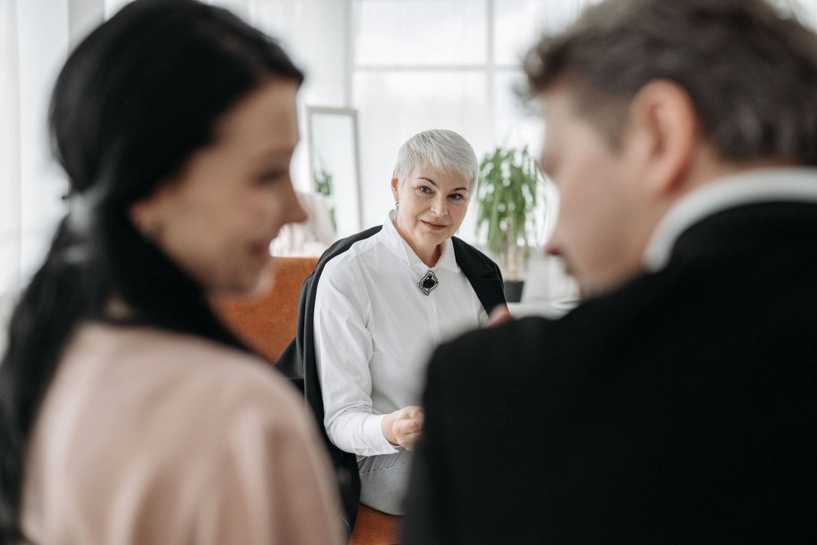 A professional woman in a white shirt speaks with a couple in a bright office