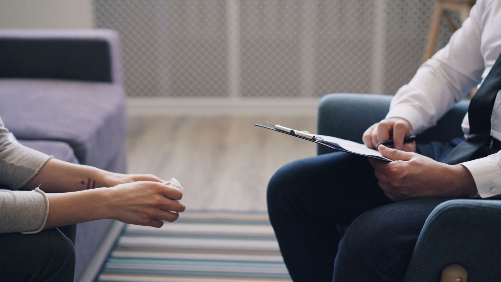 A professional with a clipboard sits across from a client on a sofa