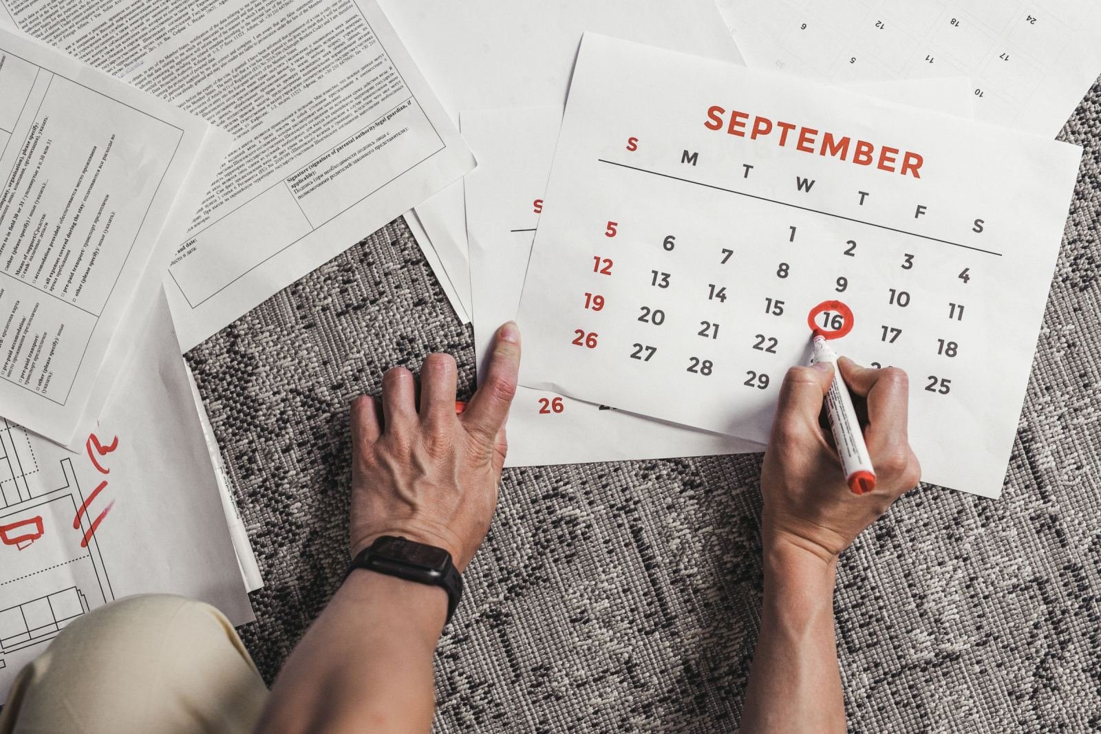 A person circles a date on a September calendar surrounded by papers