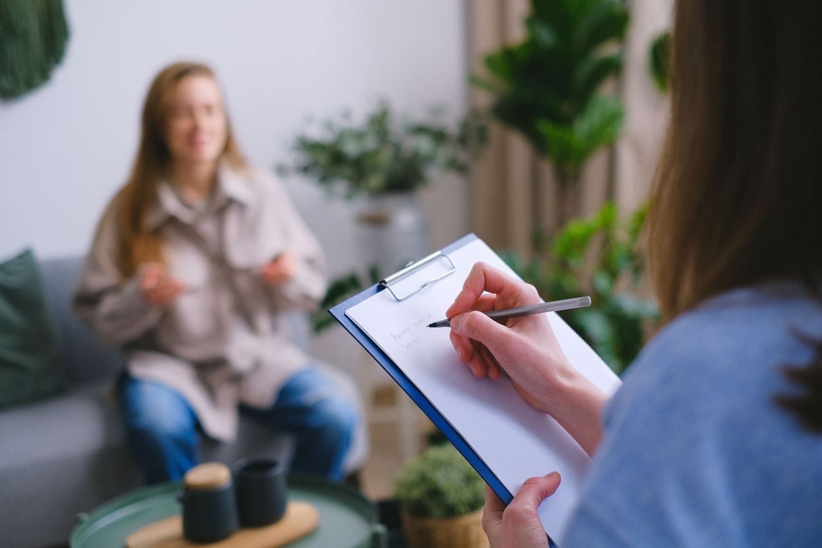 A client talks while a clinician writes notes on a clipboard in the foreground