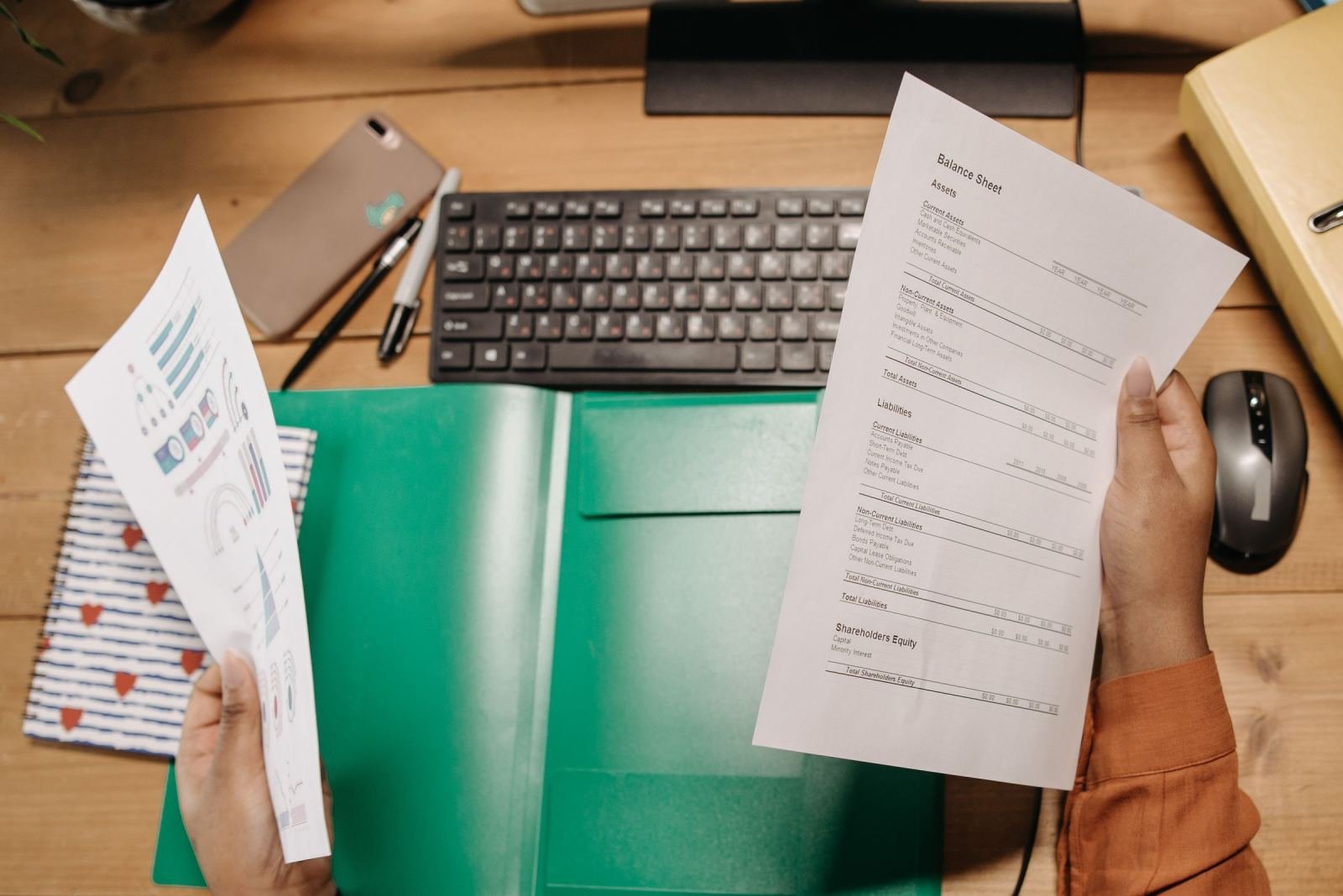 Hands holding financial documents over a desk with a keyboard and mouse