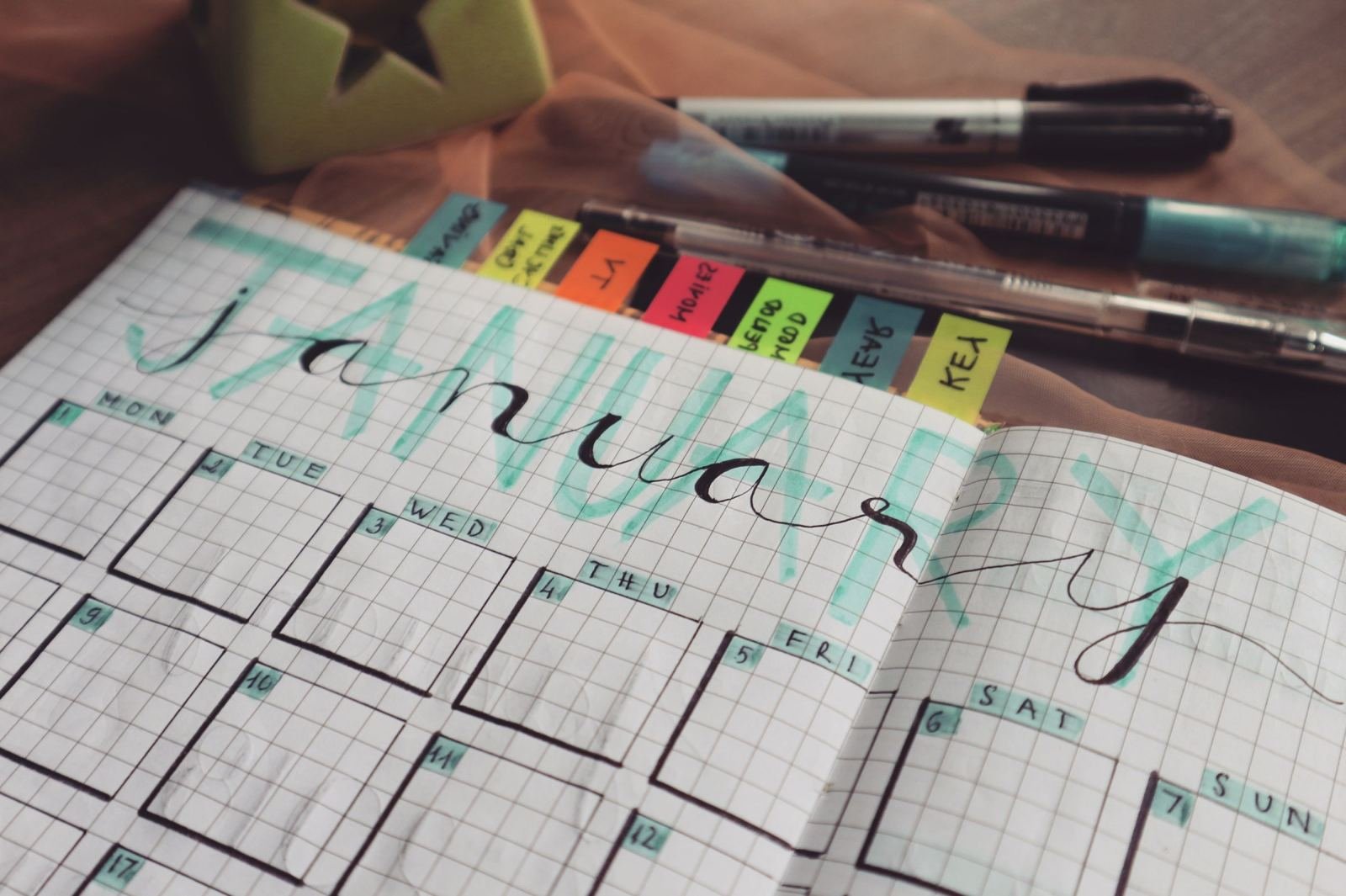 An open planner showing a January calendar drawn by hand, with bright sticky tabs