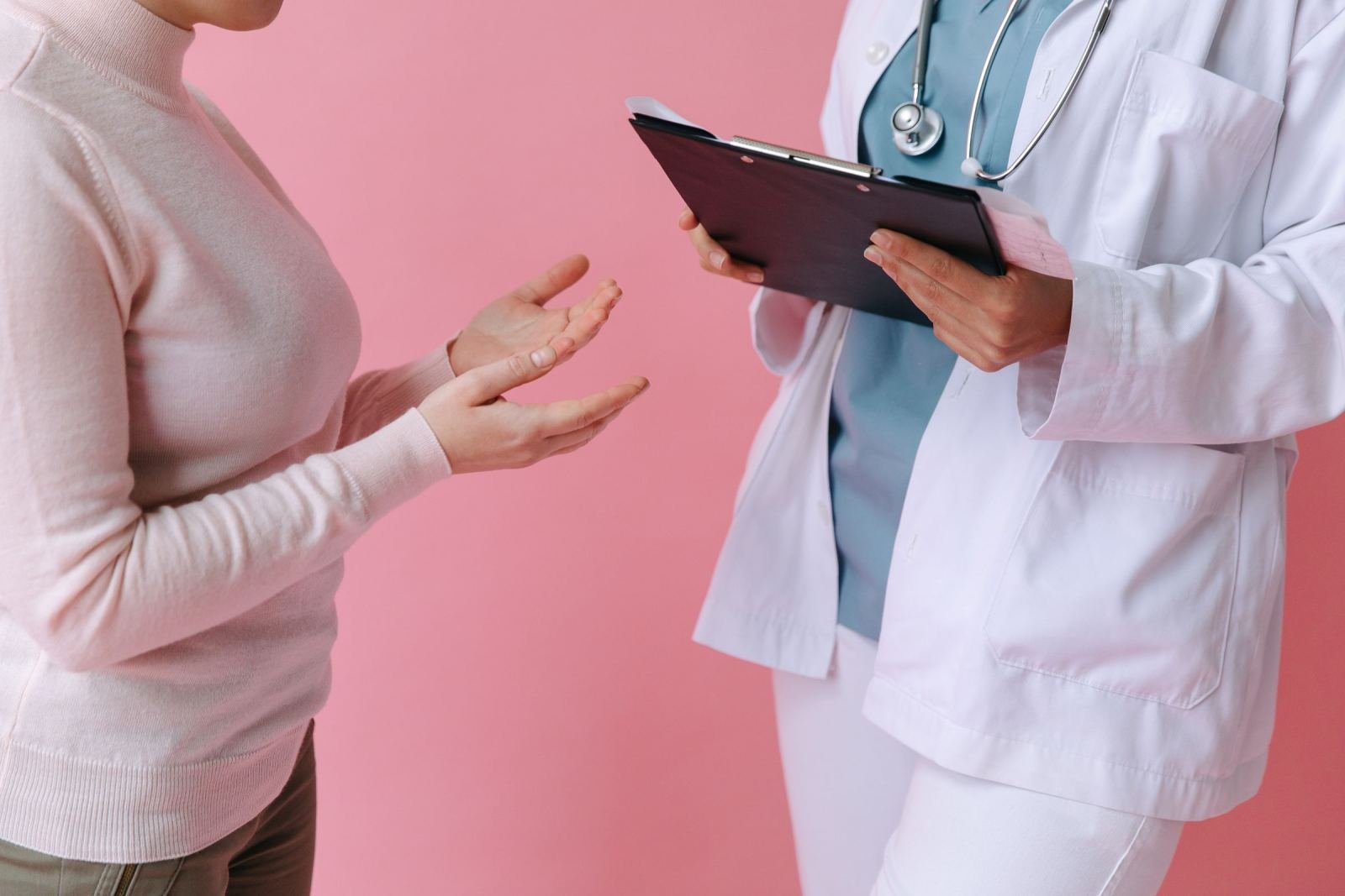 A person in a white sweater talks to a clinician holding a clipboard