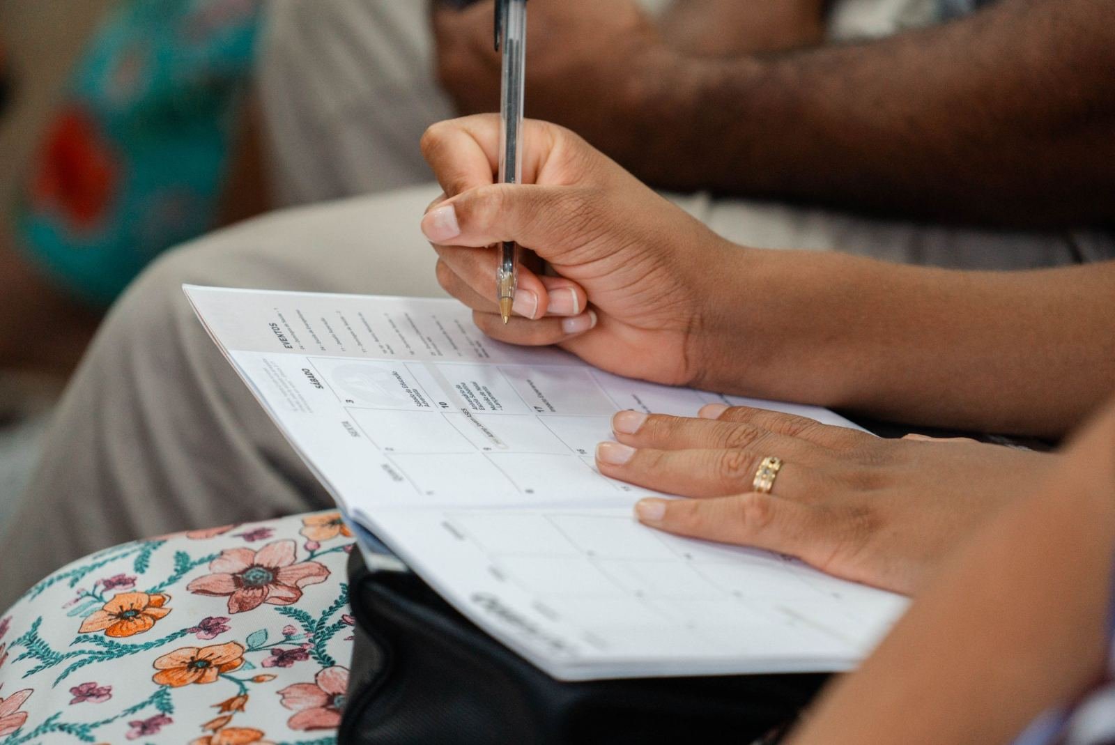 Someone marks a date on a paper calendar with a pen