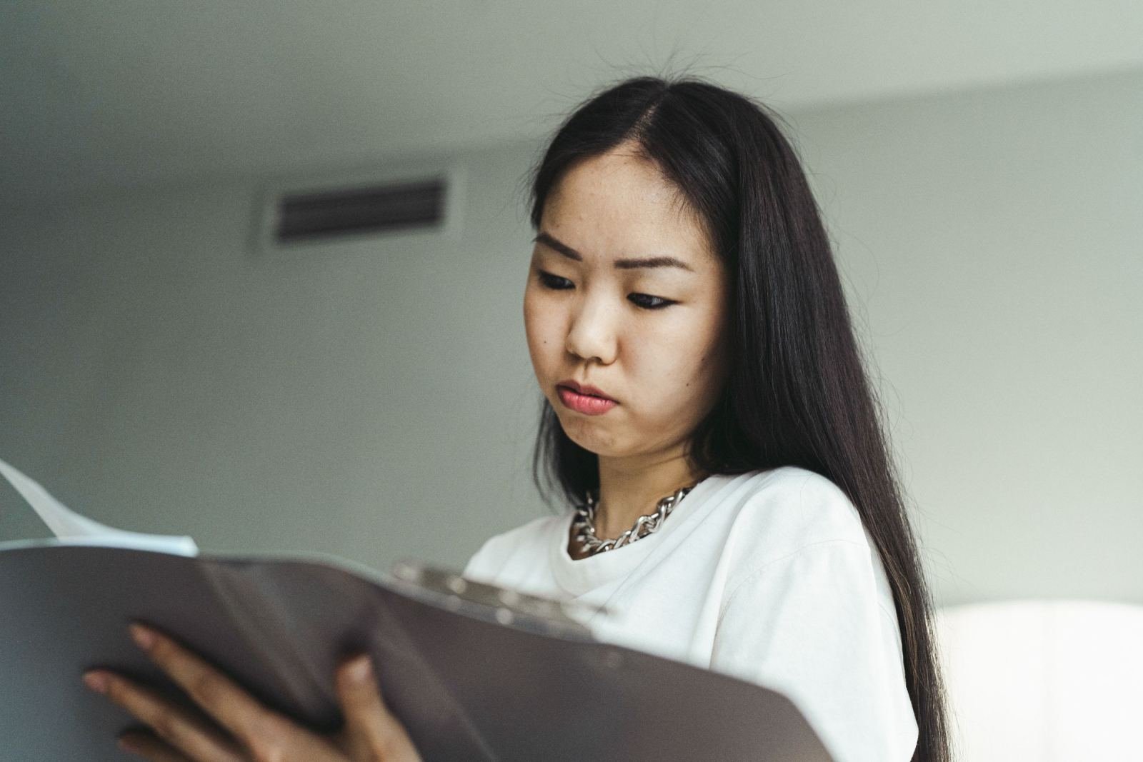 A woman looks down at a paper folder in her hands. Her face shows a serious look.
