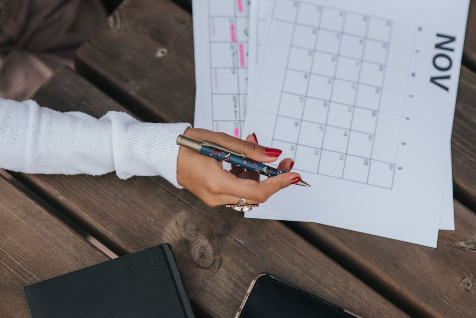 A person holds a pen over a November calendar on a wooden table