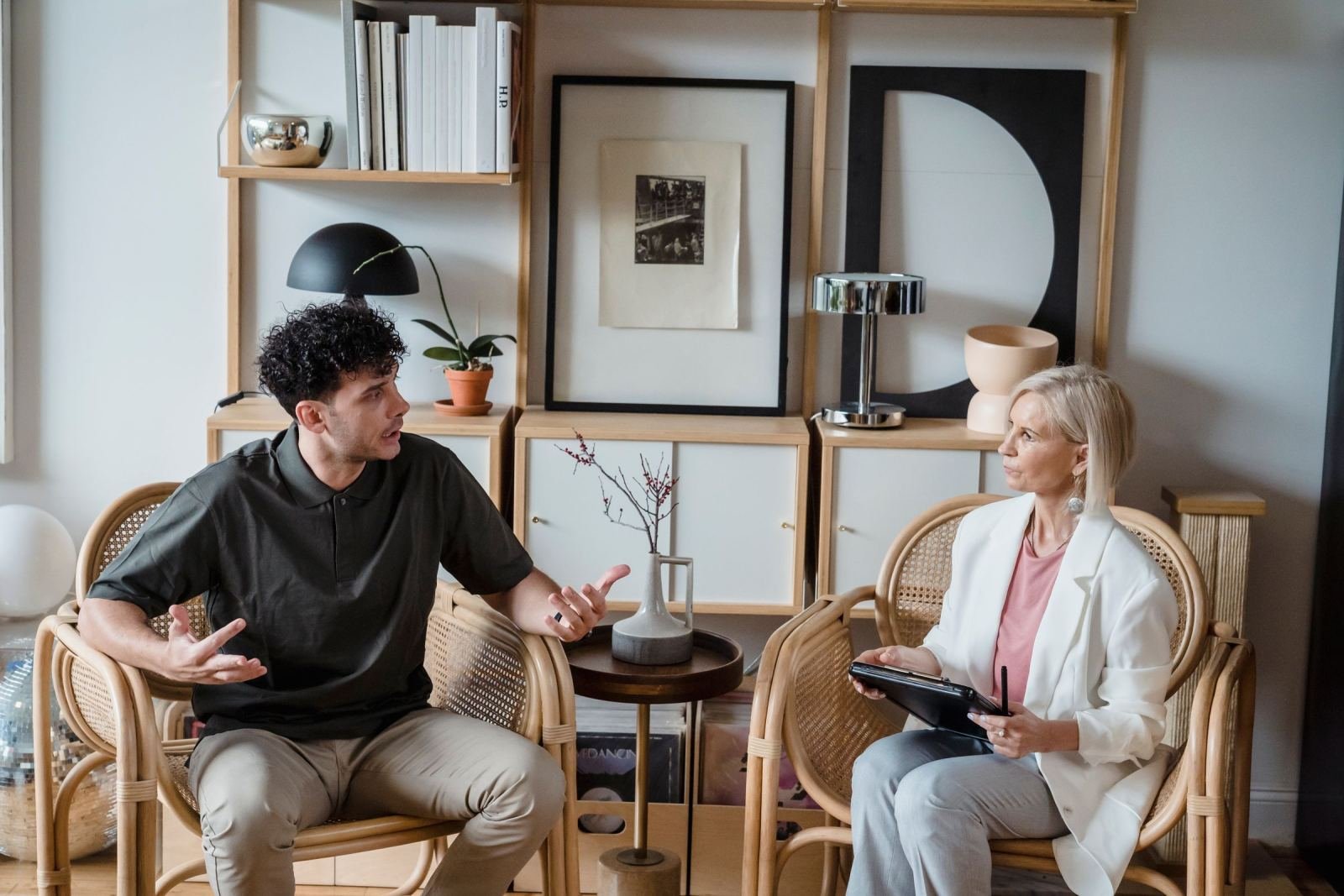 A man gestures while speaking to a woman holding a tablet in a bright office