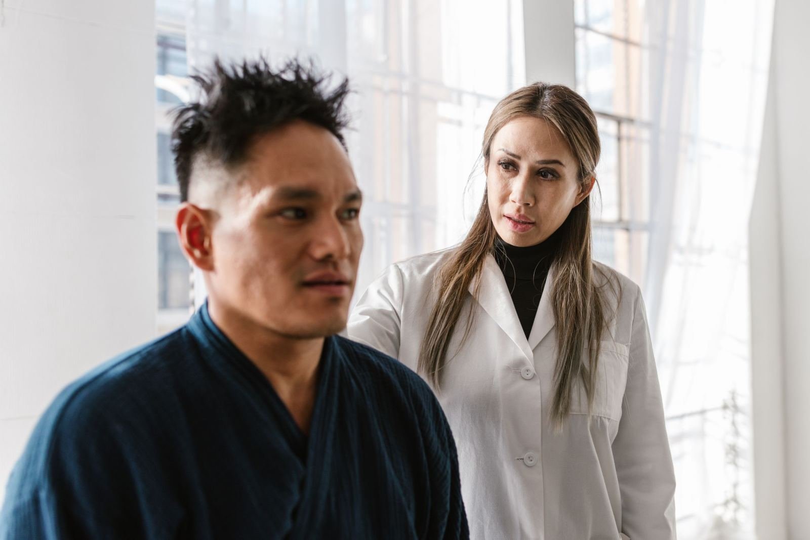 A woman in a white lab coat stands behind a man in a blue robe