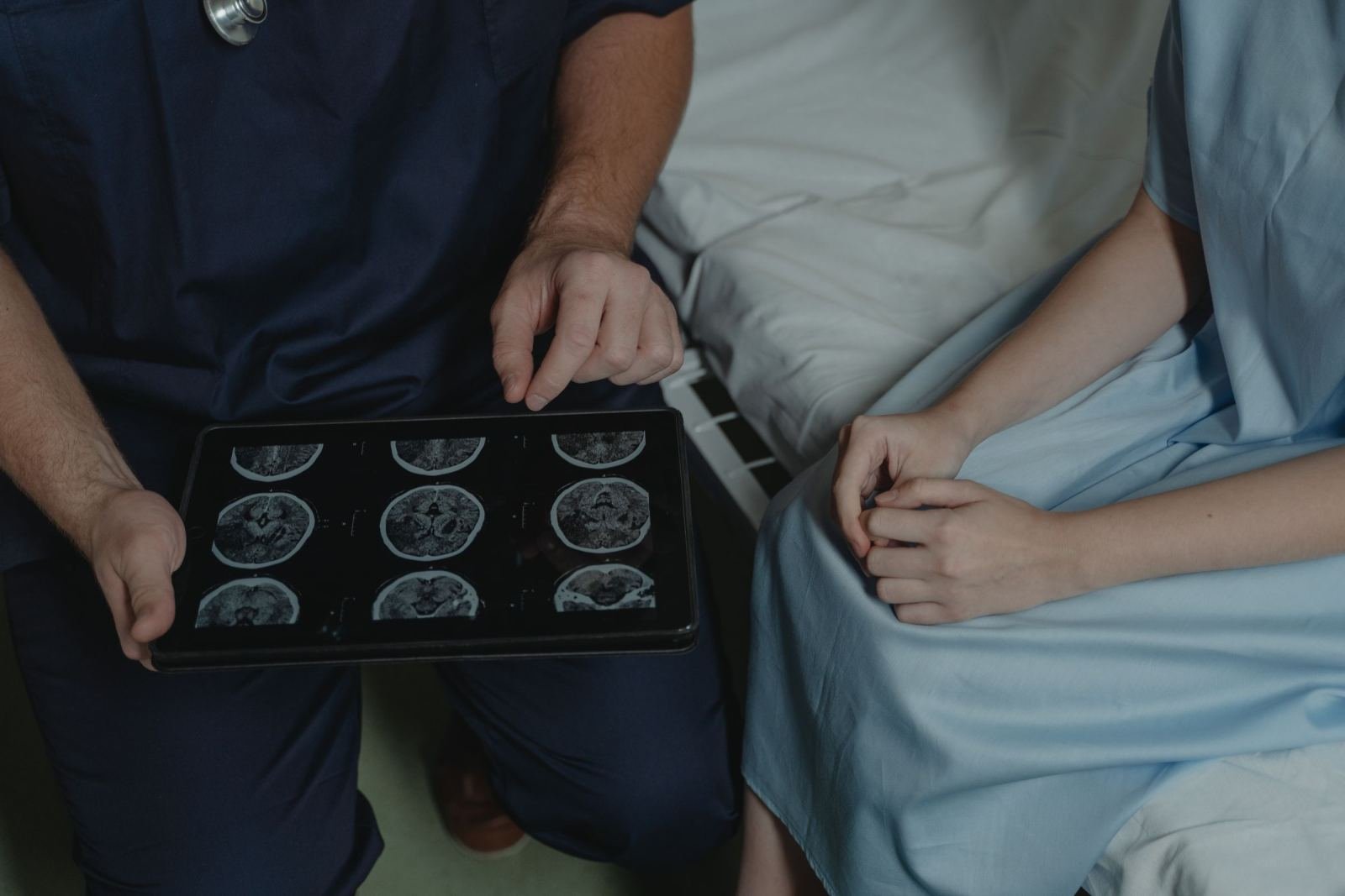 A medical professional shows brain scan images on a tablet to a patient in a hospital gown