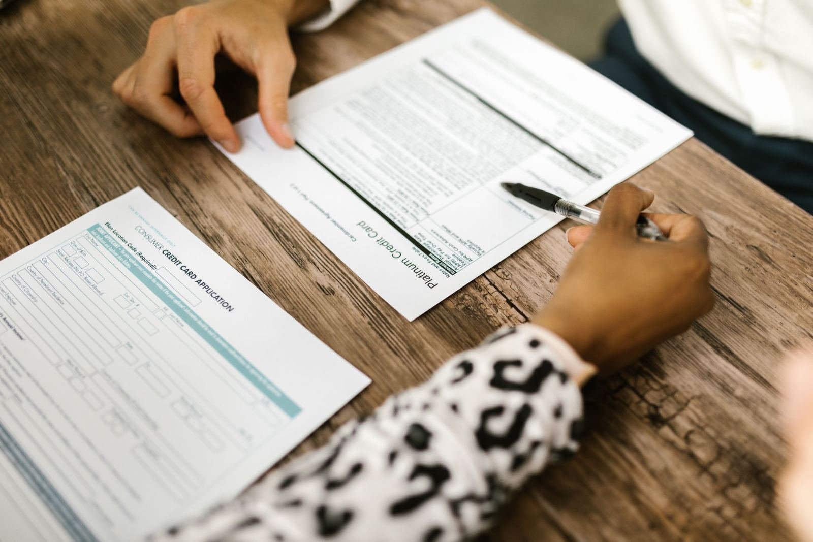 Two people look at papers on a wood desk.