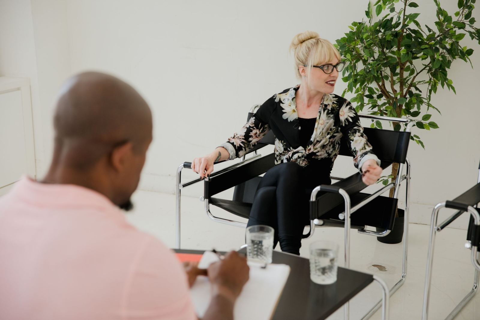 A woman in glasses speaks to a man who is taking notes on a clipboard
