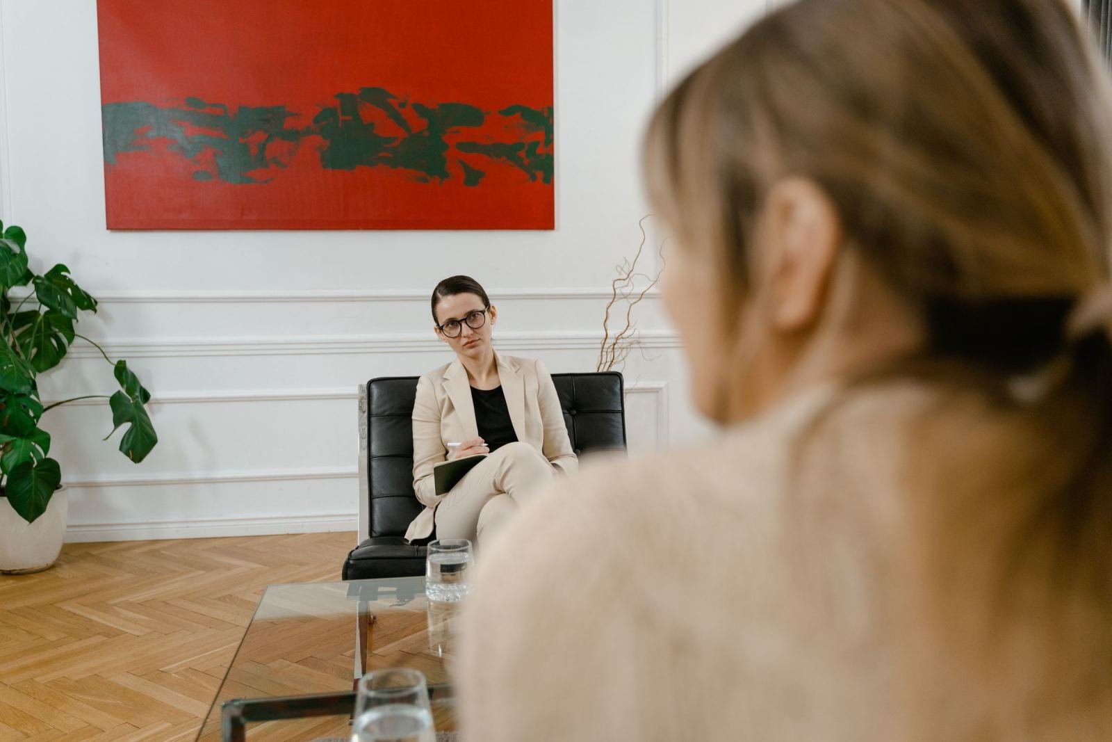 A client talks with a counselor in a beige blazer on a black sofa