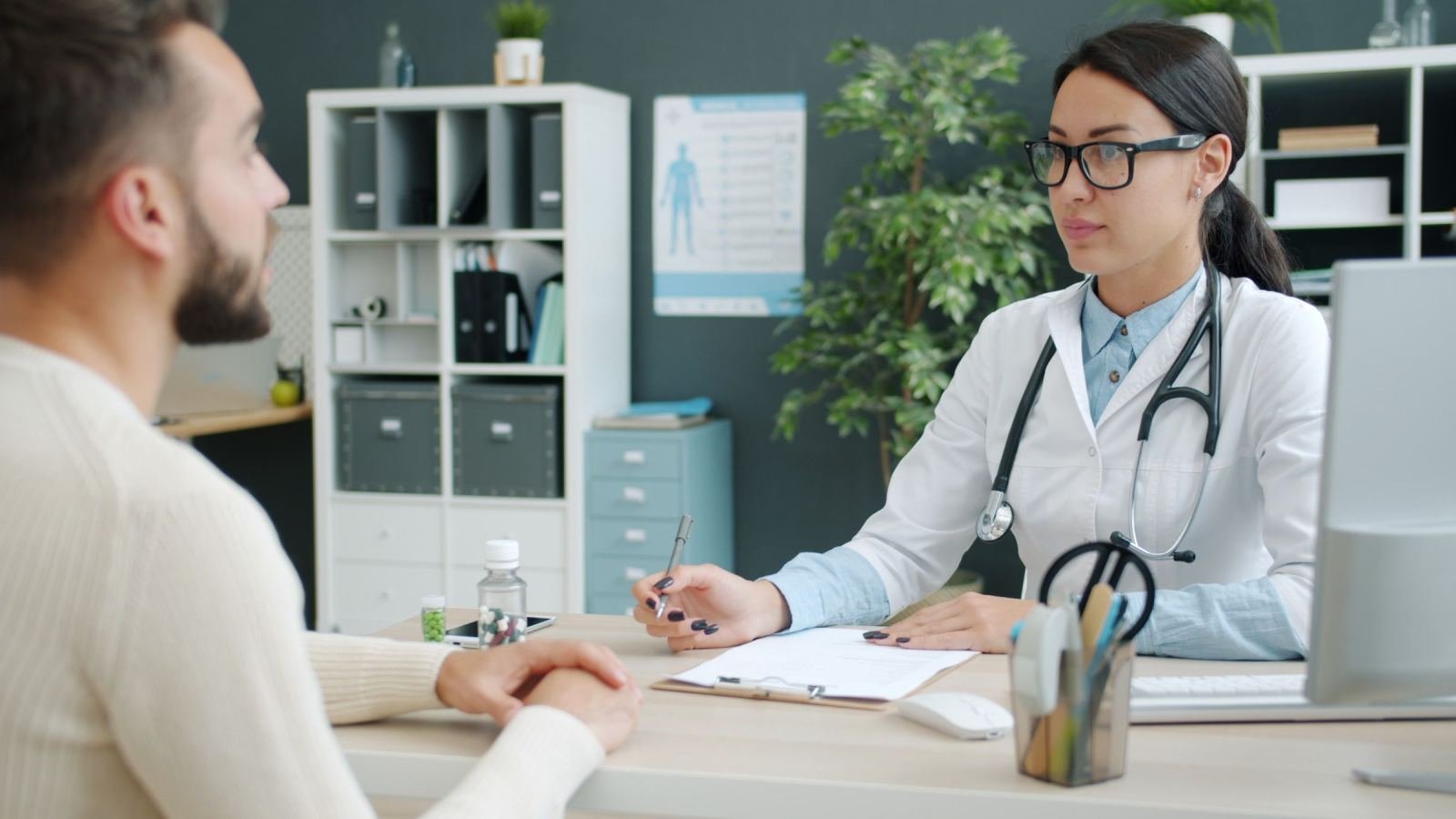A clinician in a white coat talks with a patient in a bright office
