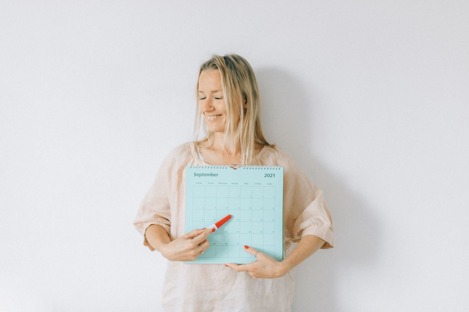 A happy woman points to a day on a blue calendar using a red marker