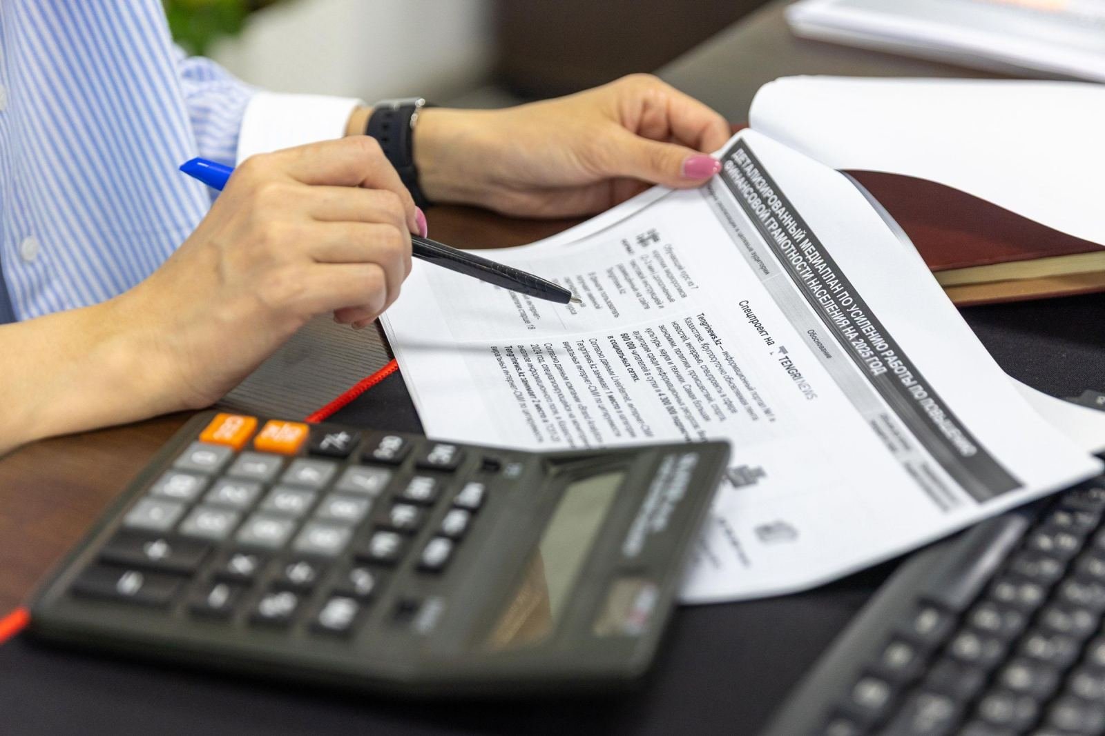 Hands using a pen and calculator to review a printed document on a desk