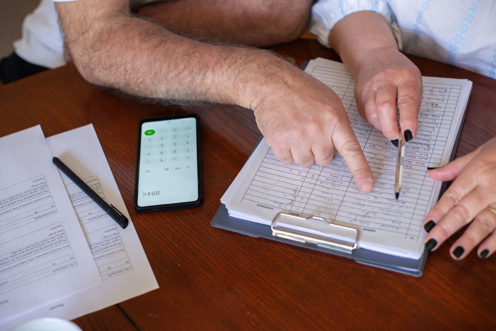 Two people review a document on a clipboard next to a smartphone calculator