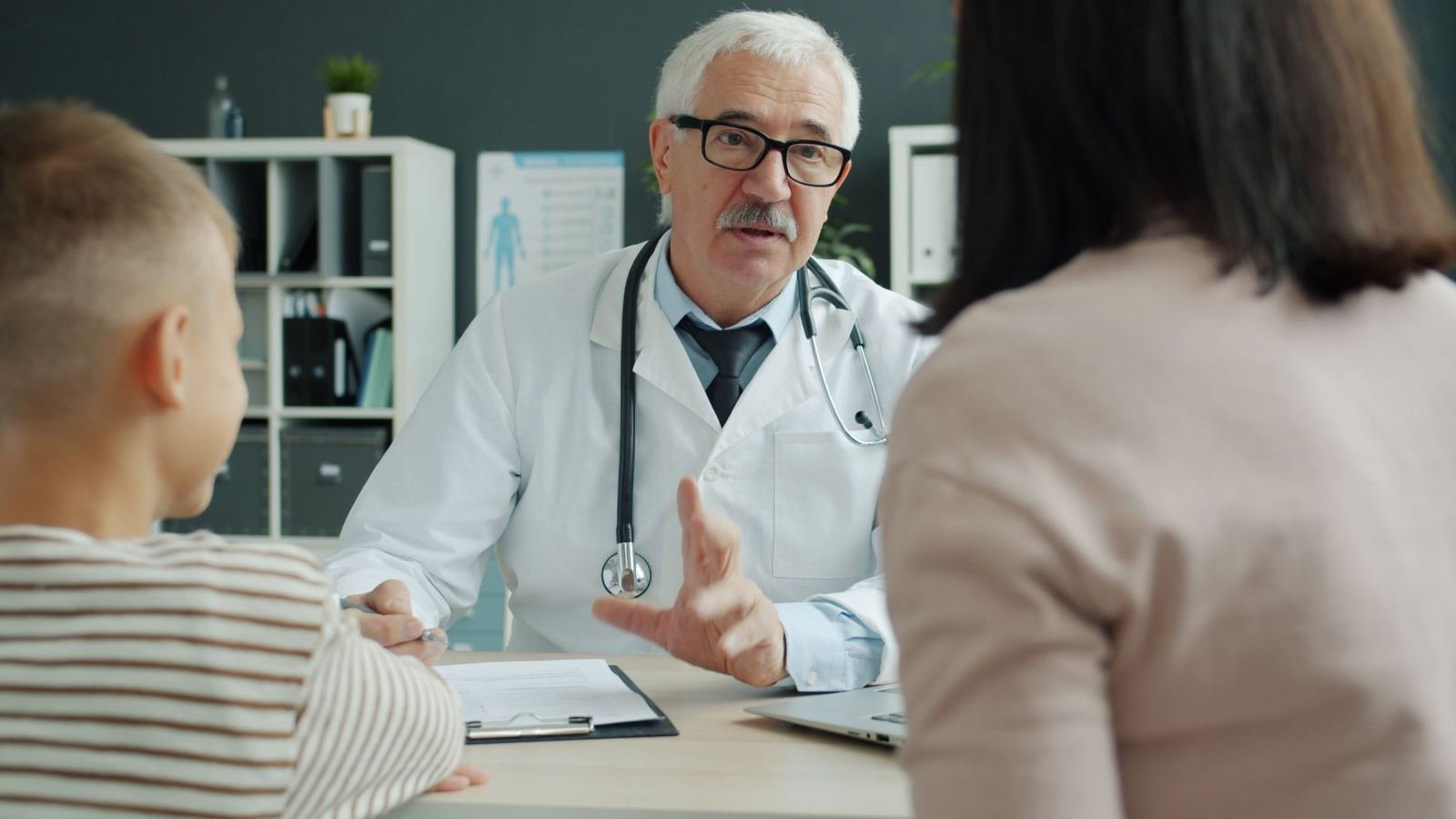 A doctor in a white coat speaks with a woman and a child in his office
