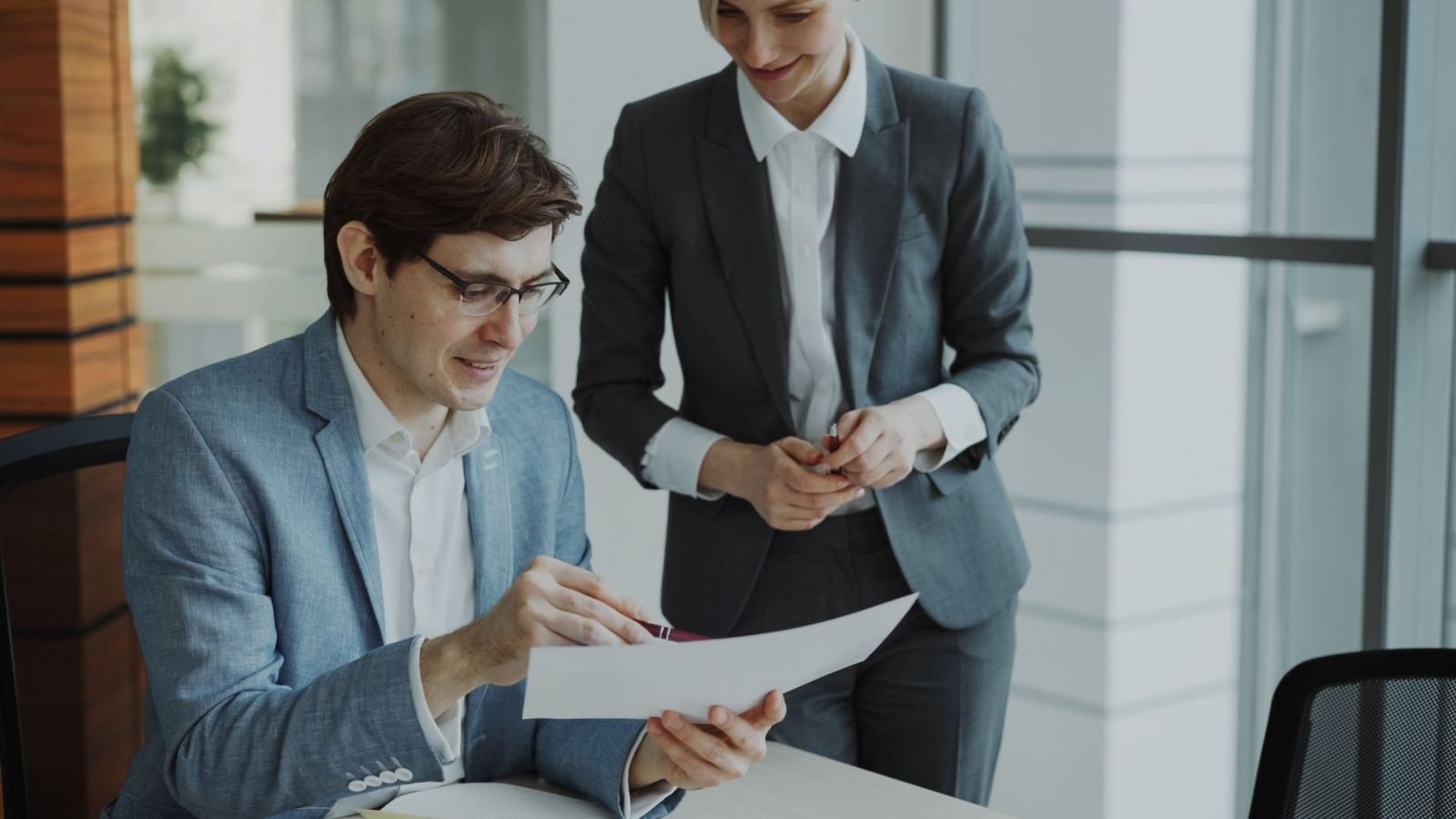 Two professionals in business clothes look over a paper together in an office.